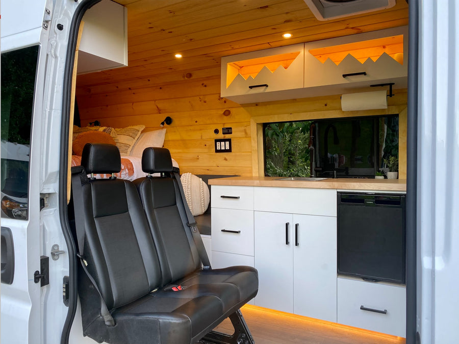 This cozy rv rental interior features a functional kitchen, comfortable bed, and passenger seating, ideal for road trips.