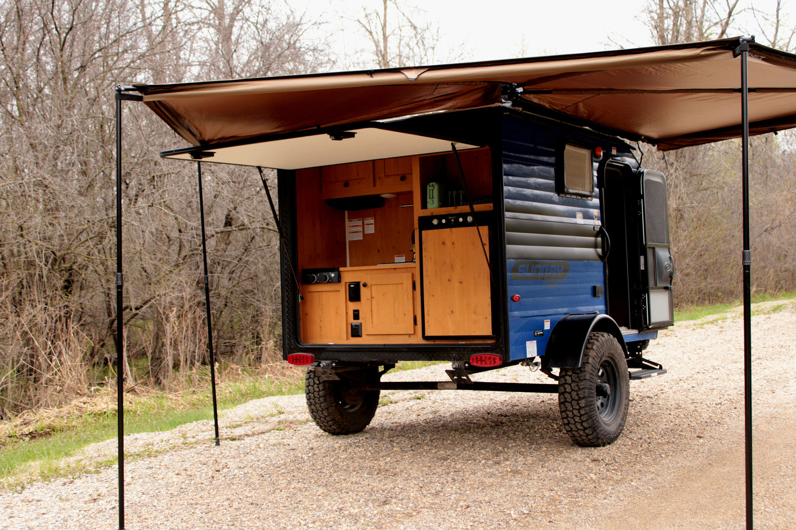 Blue off-road camper with rear outdoor kitchen & awning setup, ideal for your next RV rental camping adventure.