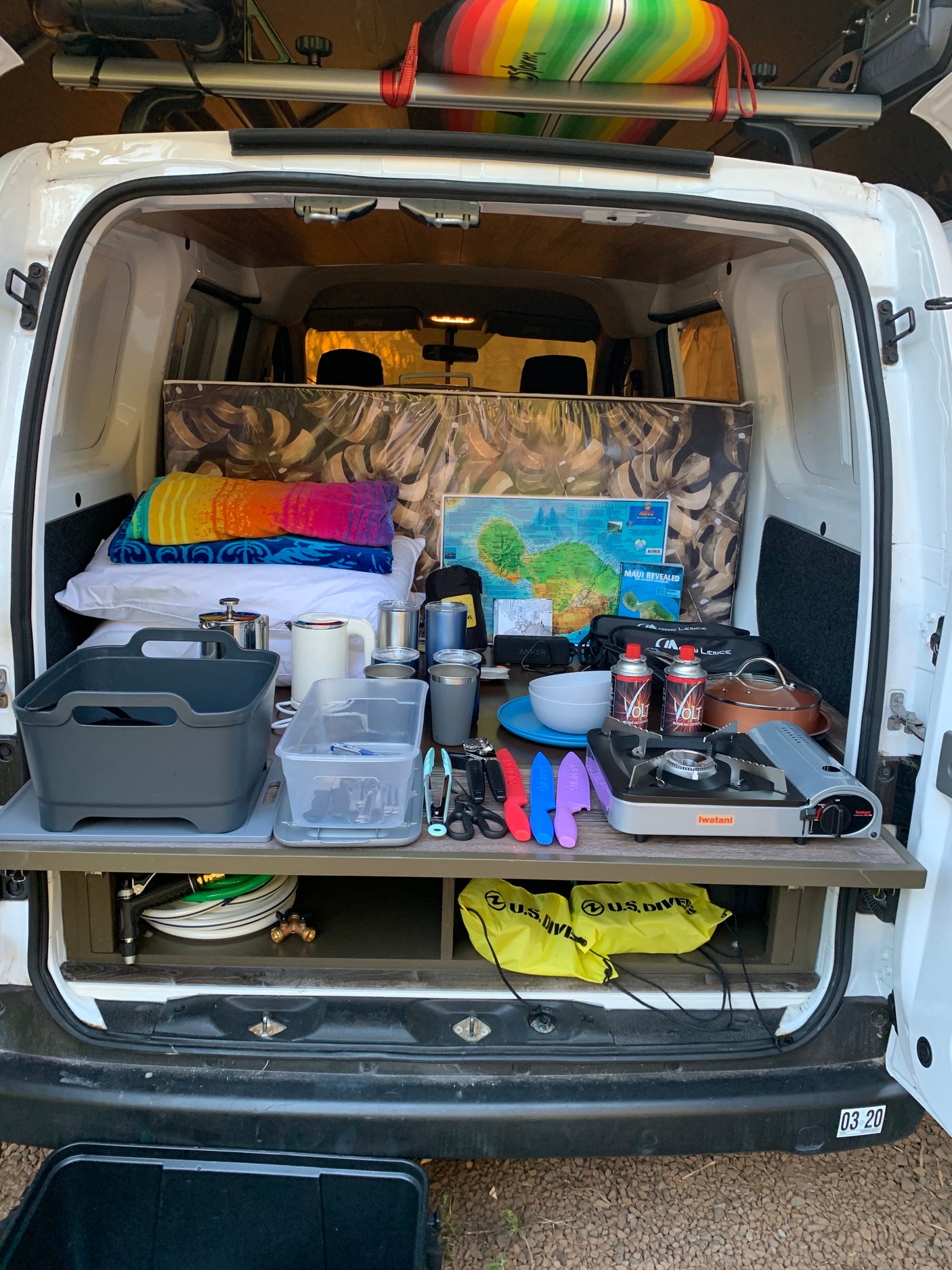 RV rental camper van interior. Organized kitchen setup, cozy sleeping area, and adventure gear including a surfboard.