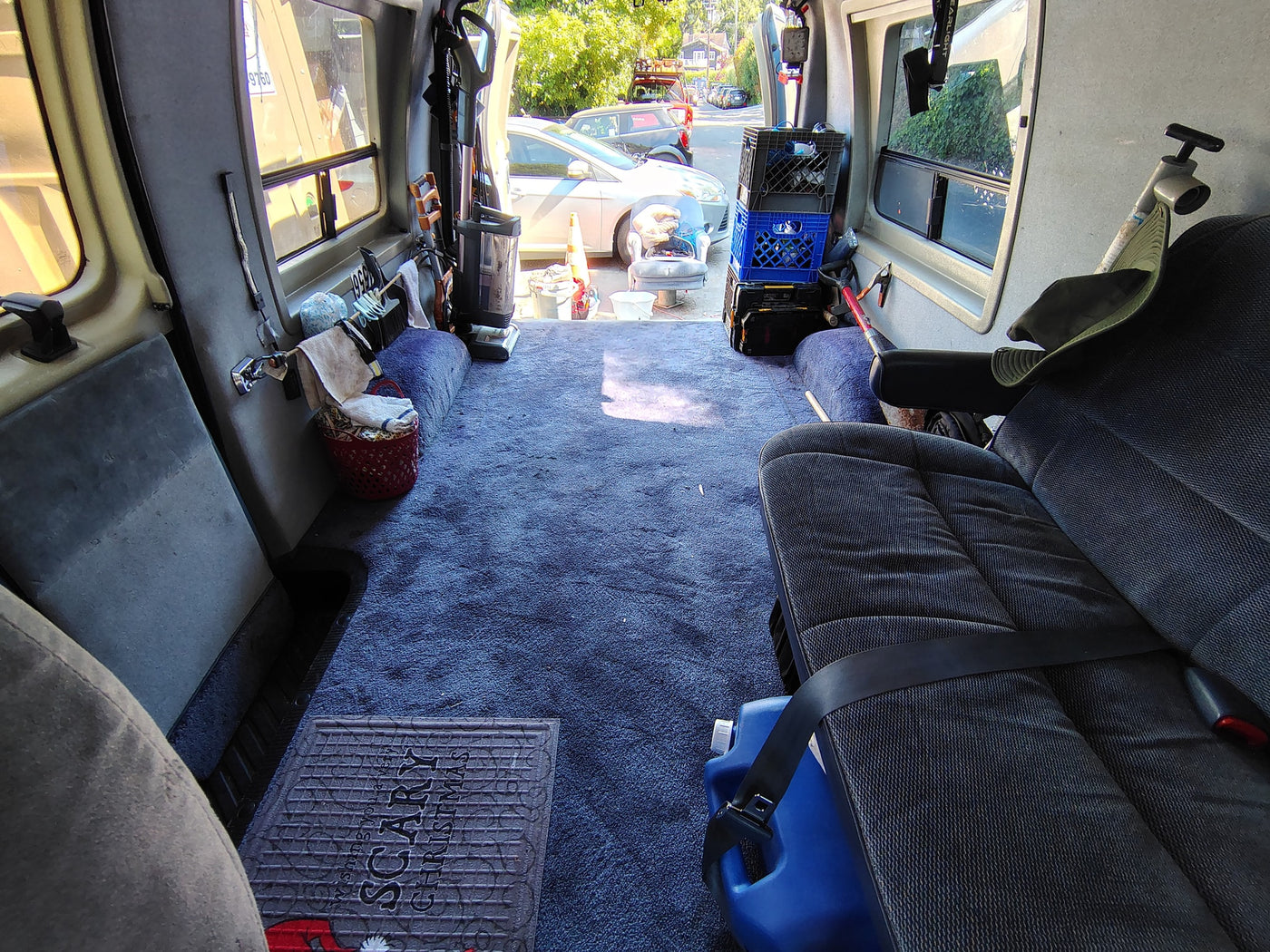 Inside an RV rental: blue carpet, passenger seat with water jug, and organized storage for mobile living. Rear door open. — photo 1
