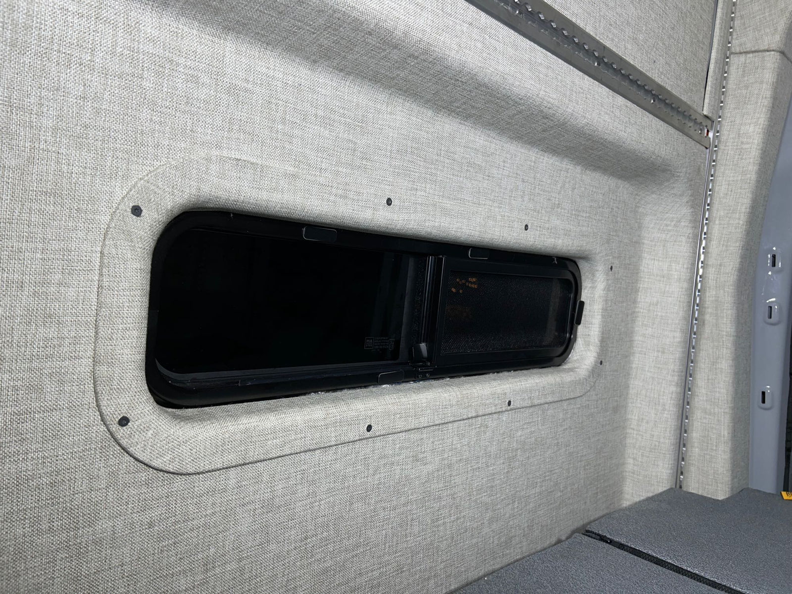RV rental camper van interior featuring soft fabric walls, a modern window, and integrated L-track storage.