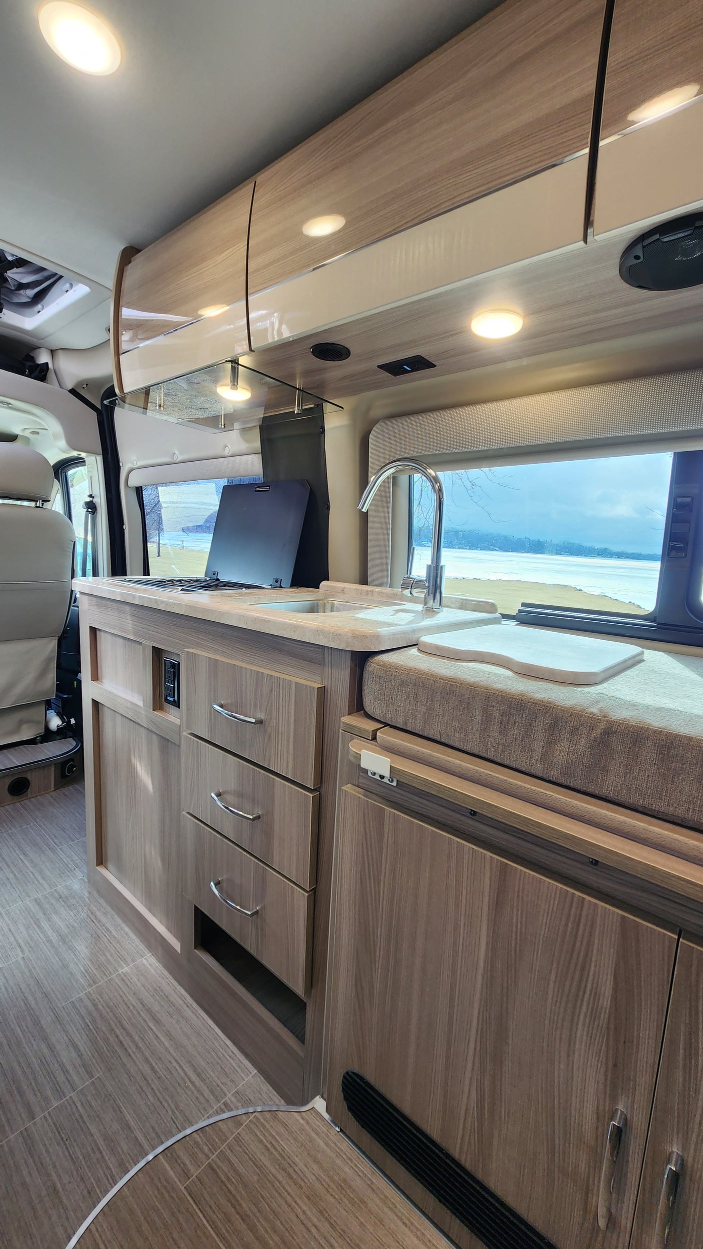 Explore this modern RV rental interior featuring a full kitchen with sink, ample storage, and a scenic window view. Comfortable travel.