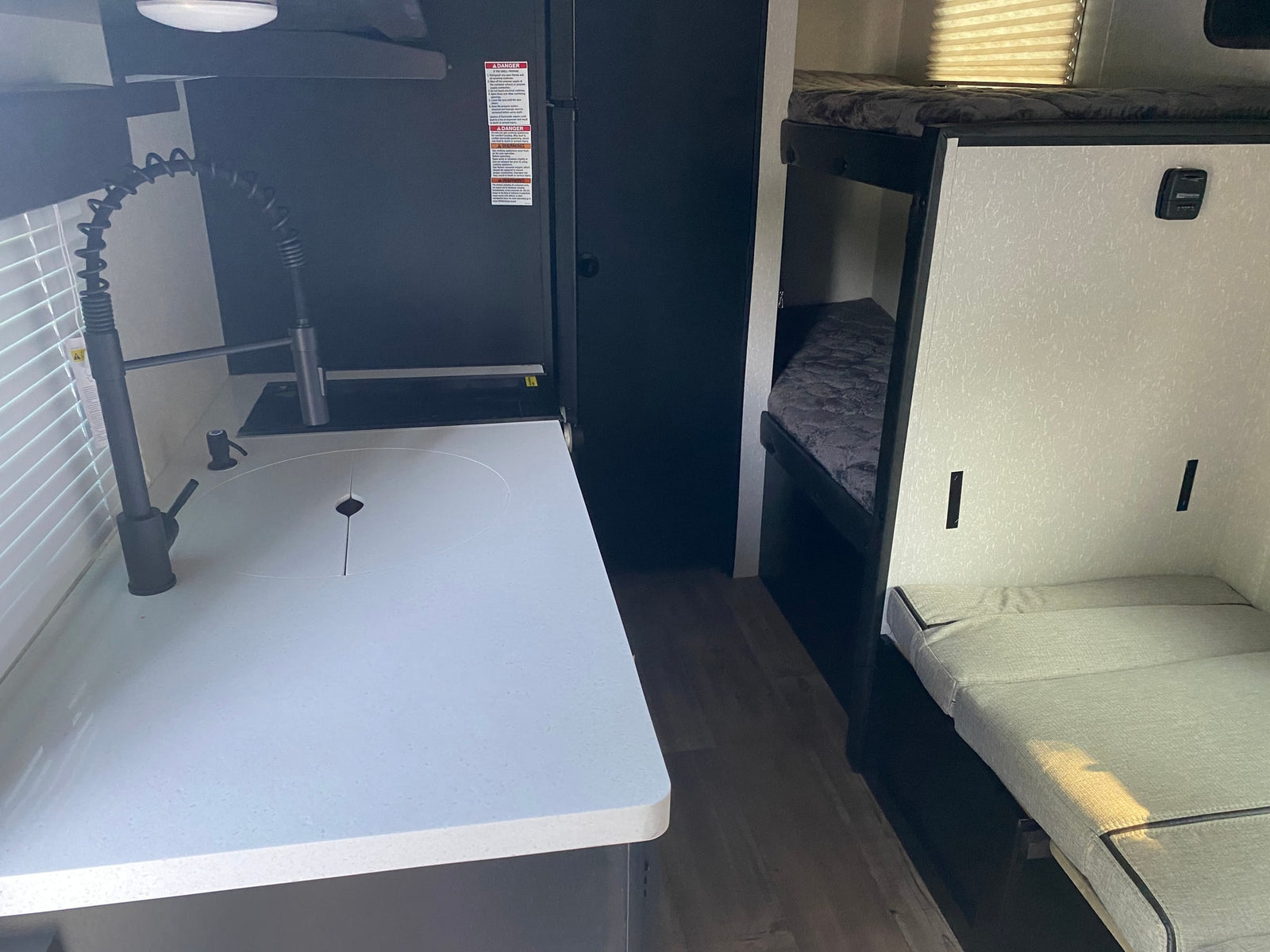 Inside an RV rental: modern kitchen with sink, black fridge, and versatile bunk beds/seating area in a compact living space.