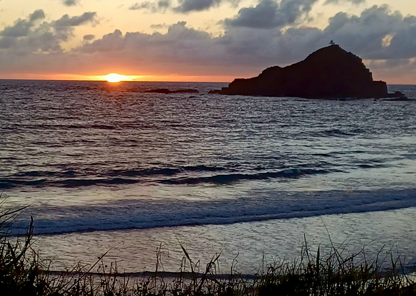 Sunset over a tranquil ocean with a silhouetted island. Plan your next RV rental escape!