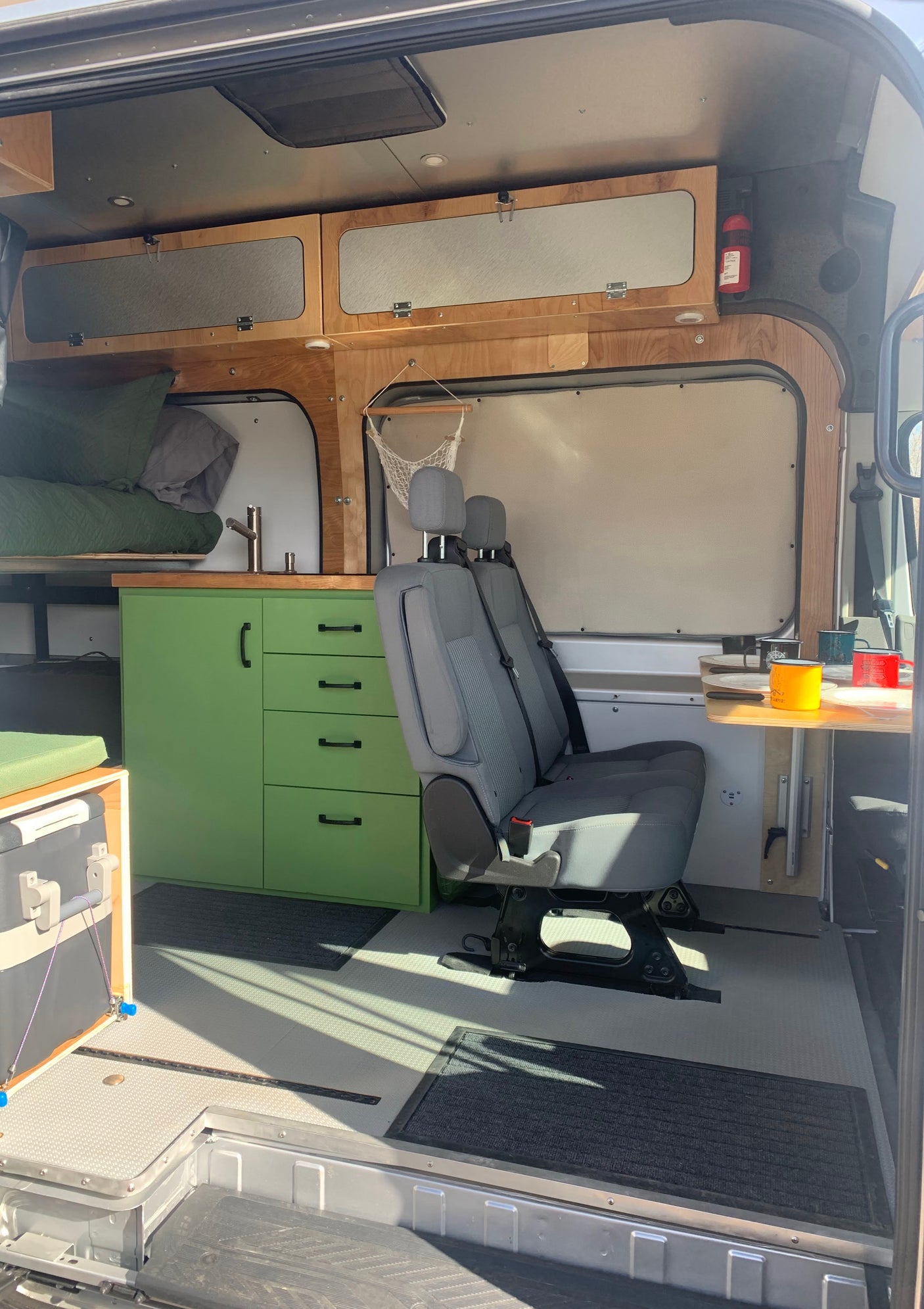 Bright and organized RV rental van interior with green kitchen, bed, passenger seating, and ample overhead storage.