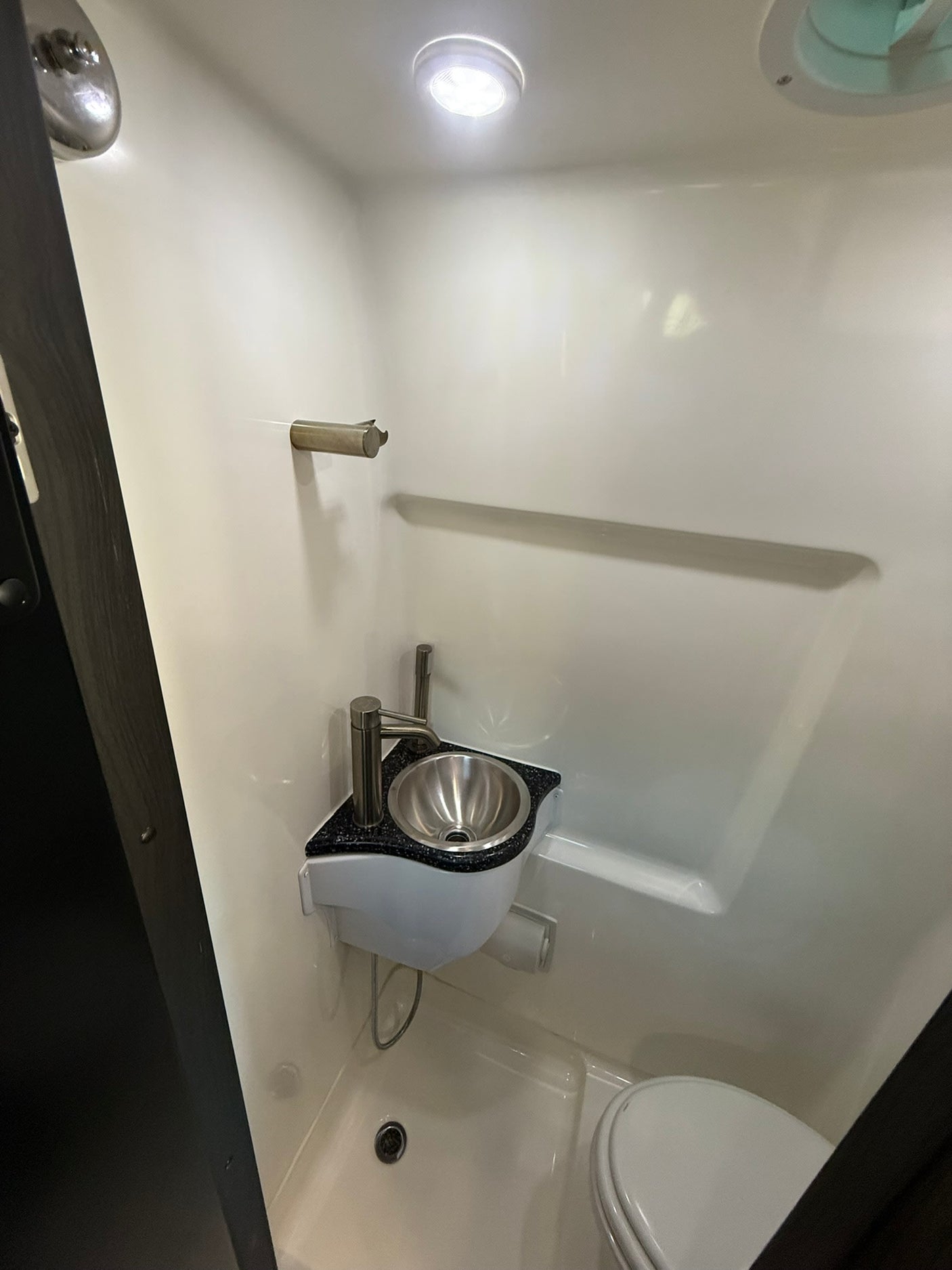 Compact RV rental wet bath: Features a toilet, small sink, shower, and towel bar within a molded white enclosure.
