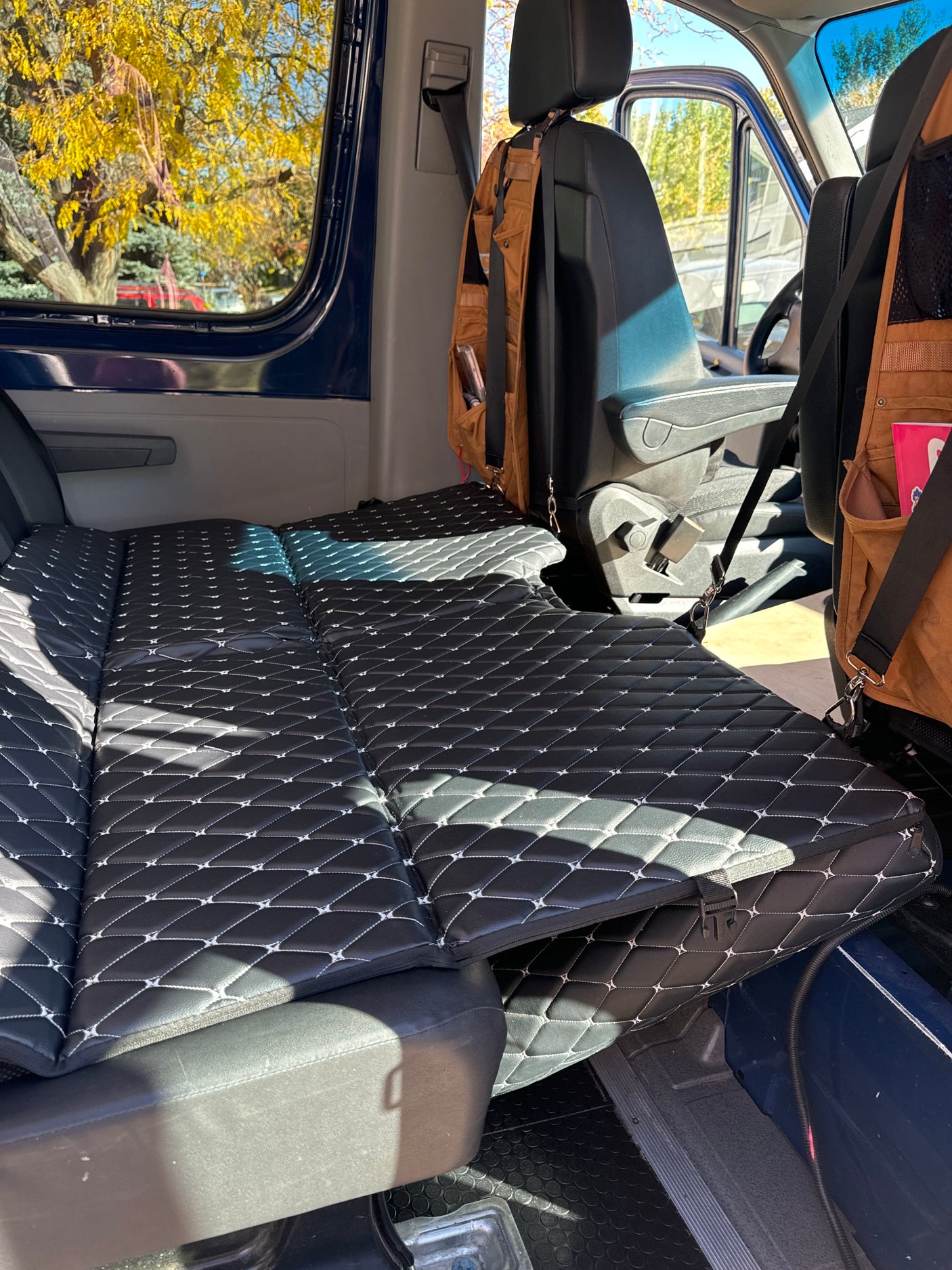 Black quilted mattress fills this RV rental van's interior, showing autumn leaves outside. Ready for adventure!