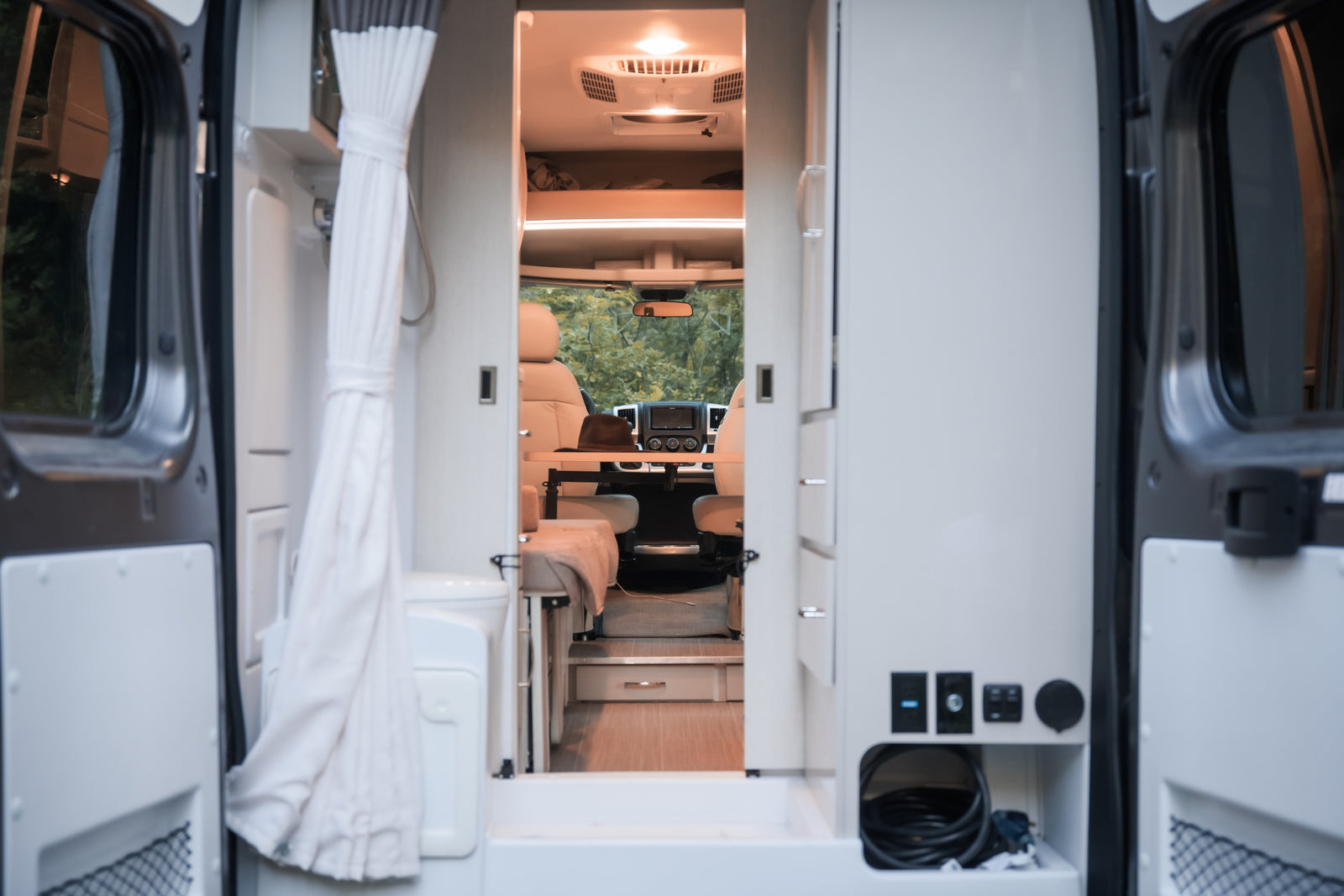 Experience comfortable rv rental adventures! View inside a camper van from open rear doors, showing the living area, bathroom, and front cab.