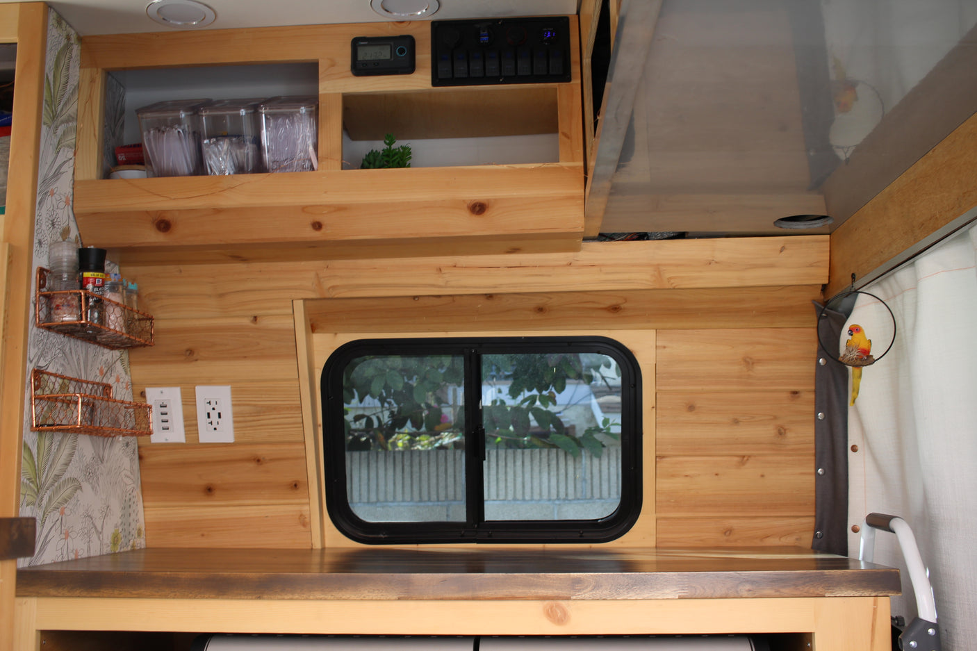 Inside a stylish rv rental: light wood paneling, counter, shelves, and a large window create a functional and cozy space.