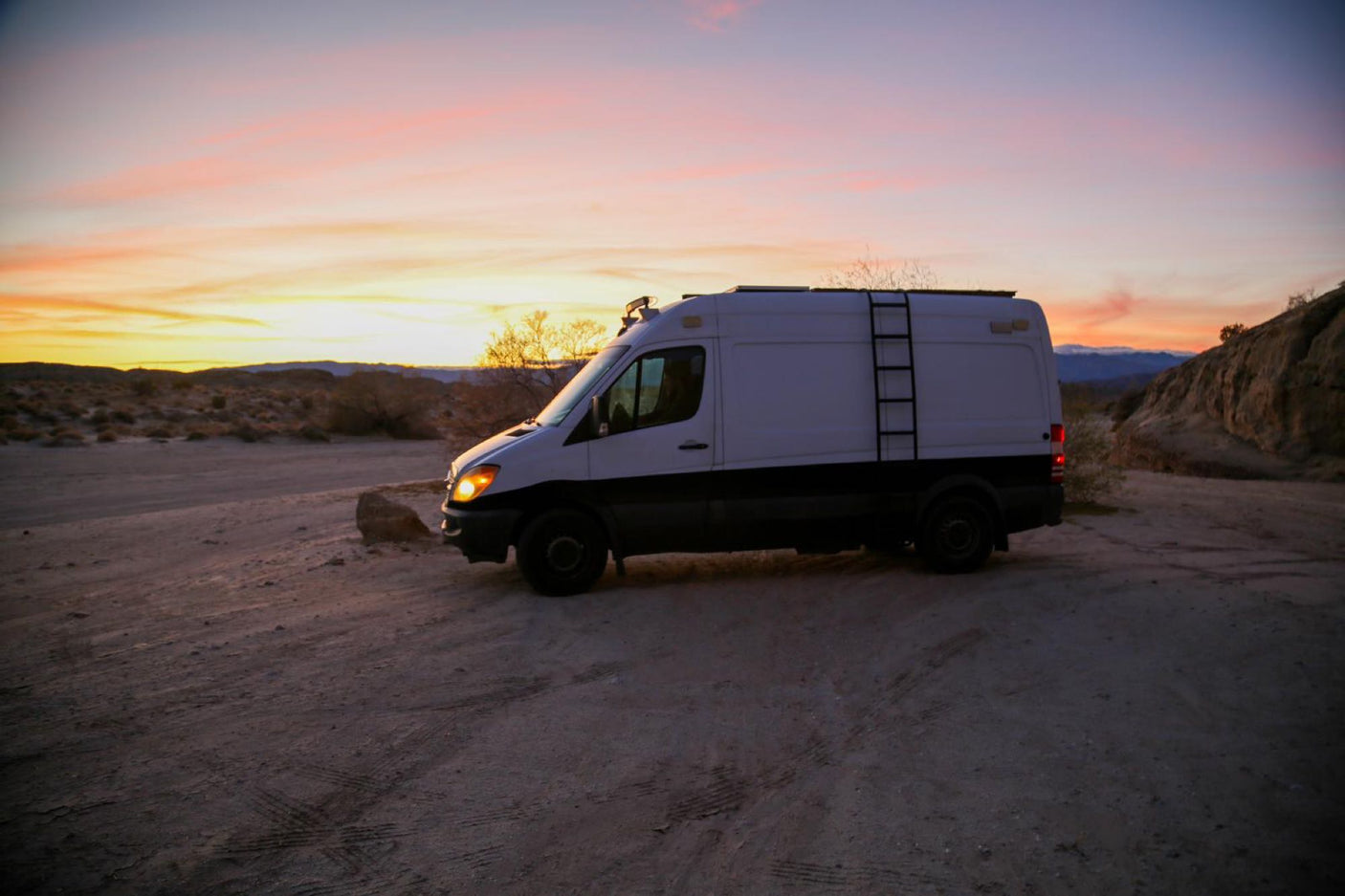 Experience van life! White RV rental van parked in a scenic desert setting under a stunning sunset sky.