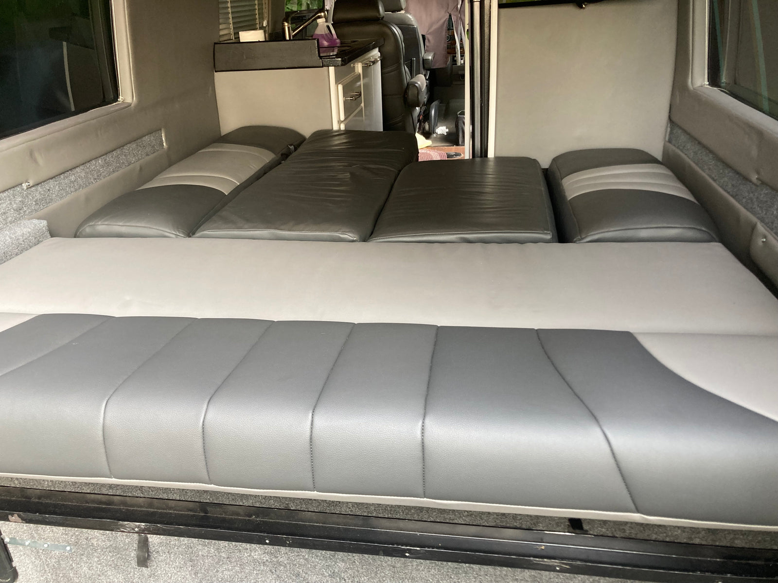 Spacious gray and white RV rental camper van interior. Features a convertible bed/seating setup and a compact kitchen.