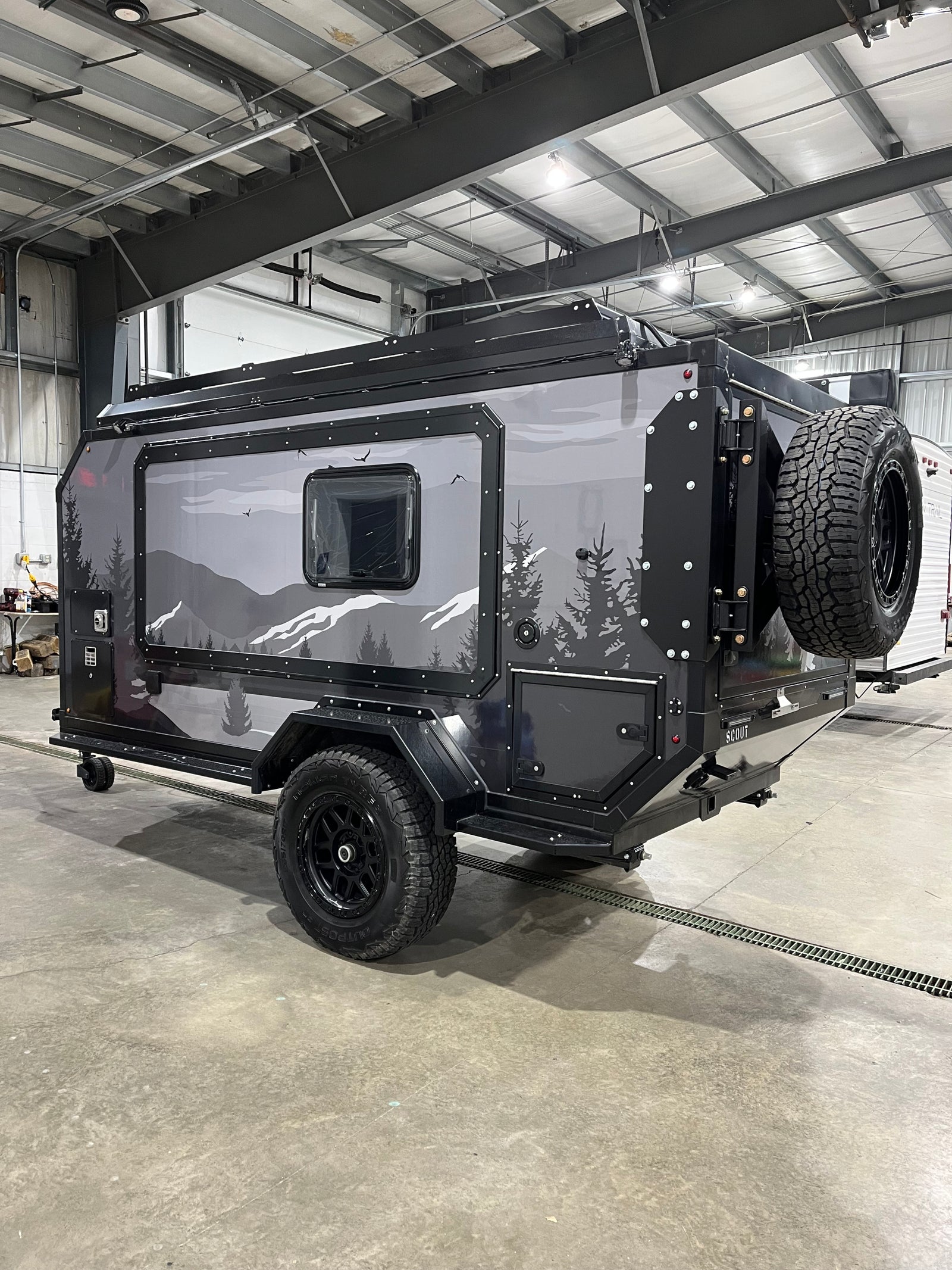 A rugged off-road camper trailer, ideal for rv rental adventures. Features unique mountain graphics and a rear-mounted spare tire.