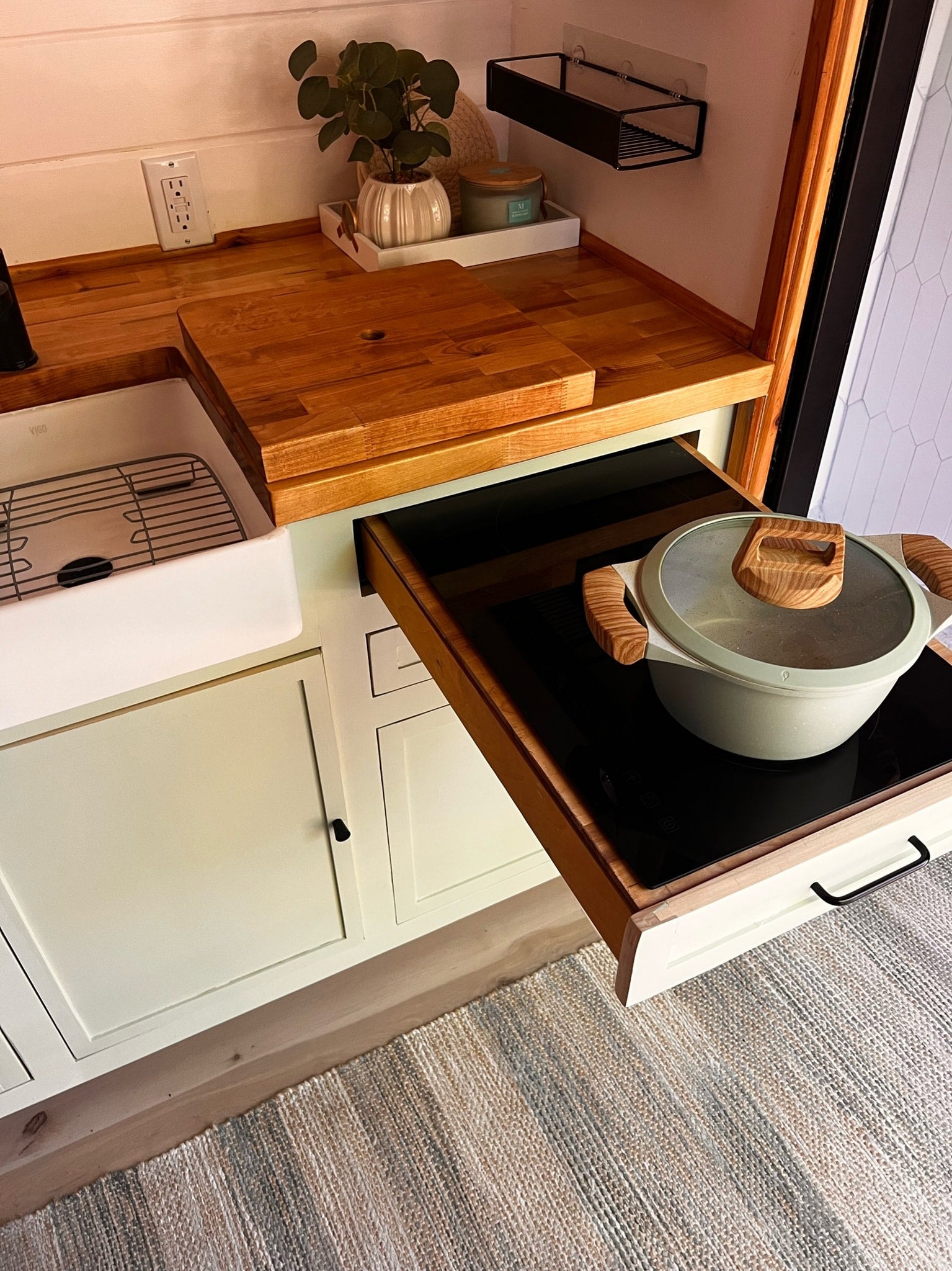 This RV rental kitchen features a clever pull-out induction cooktop, a white sink, and warm wood counters, optimizing space for mobile living.