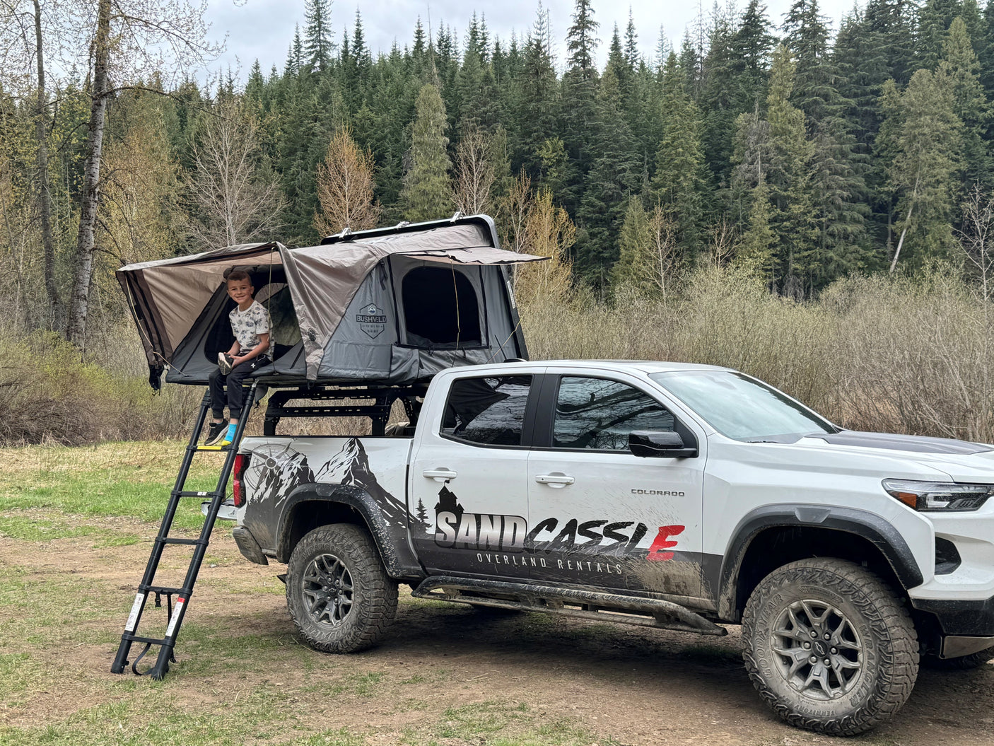 Boy smiles from a rooftop tent on a specialized pickup truck, ideal for rv rental adventures & overlanding.
