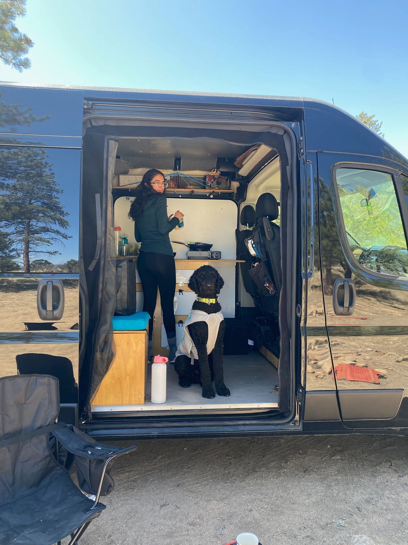 A person stands inside an open black RV rental with a dog, ready for adventure outdoors.