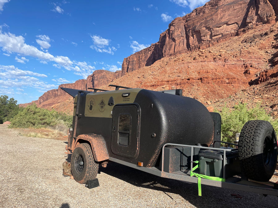 Rugged black teardrop RV rental parked against stunning red desert mountains. Ideal for off-road camping and adventure travel.|Portable hot water heater setup with propane tank for an rv rental