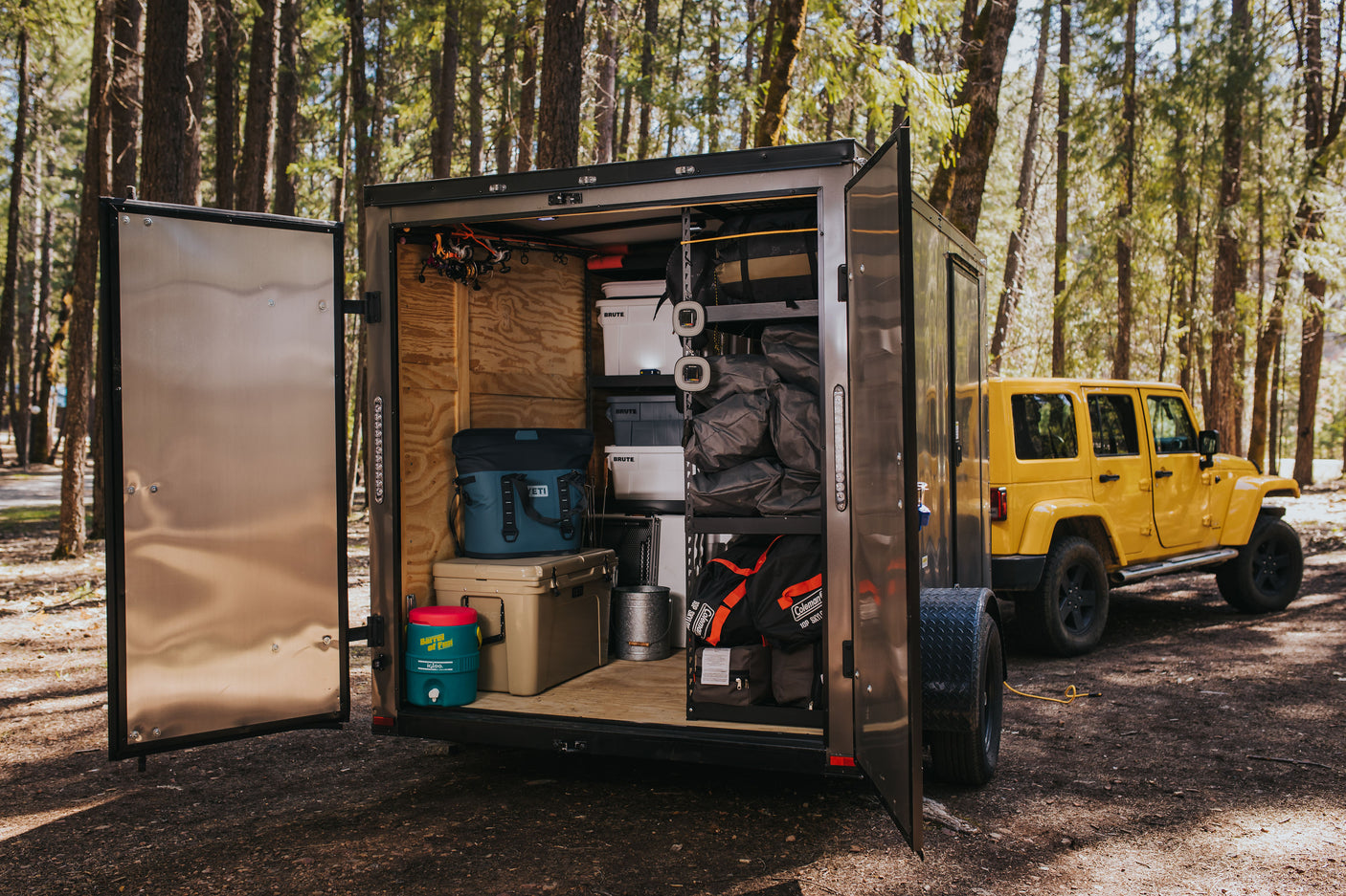 A custom camping trailer, packed with gear like Yeti coolers & Coleman sleeping bags, towed by a Jeep. Ideal for an RV rental alternative.