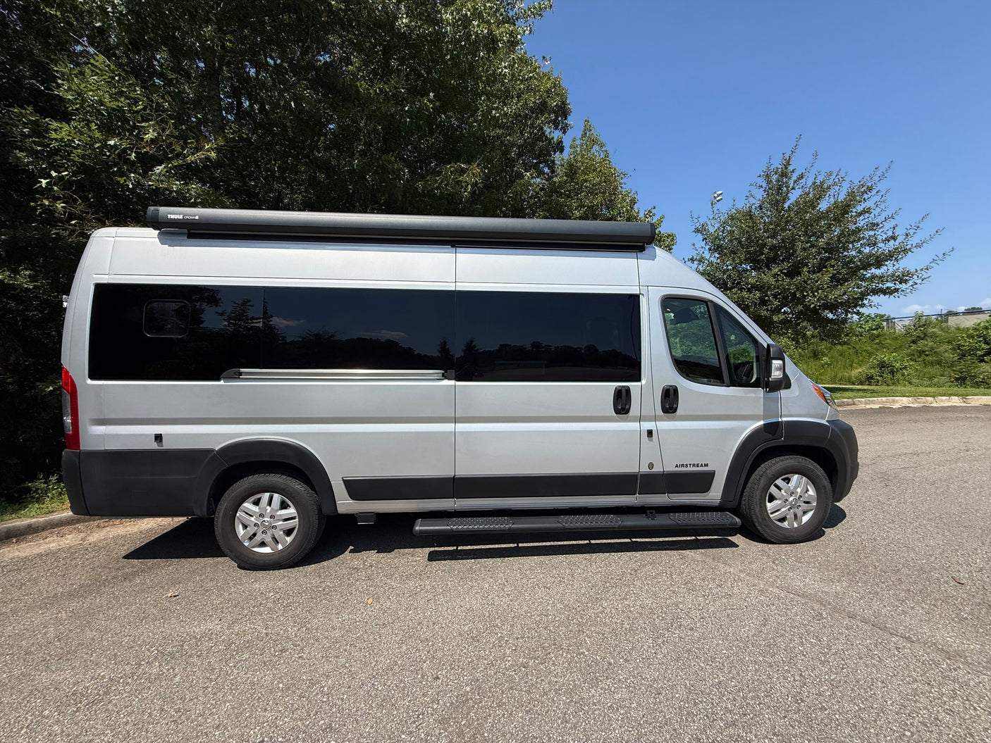 A sleek silver Airstream camper van, equipped with a Thule awning and side steps, is ideal for your next RV rental adventure.