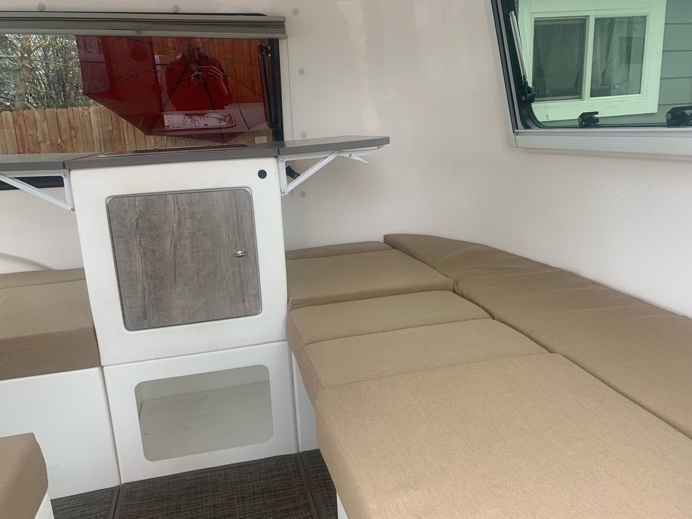 Compact RV rental interior featuring a kitchenette with fold-out table, comfy bench seating, and ample light from side windows.