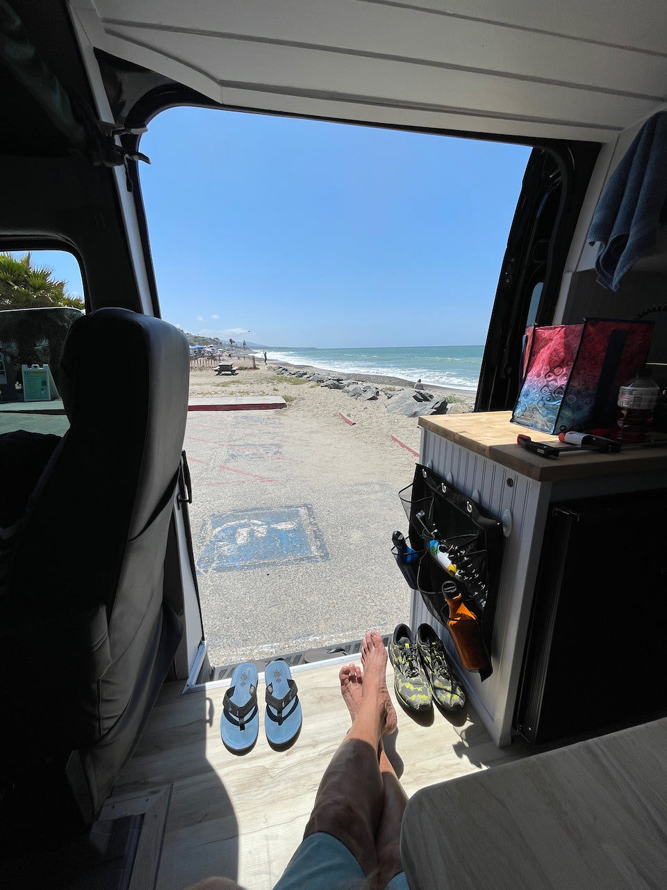 Stunning beach view from an RV rental. Legs stretched, flip-flops nearby, waves crashing. Perfect day!