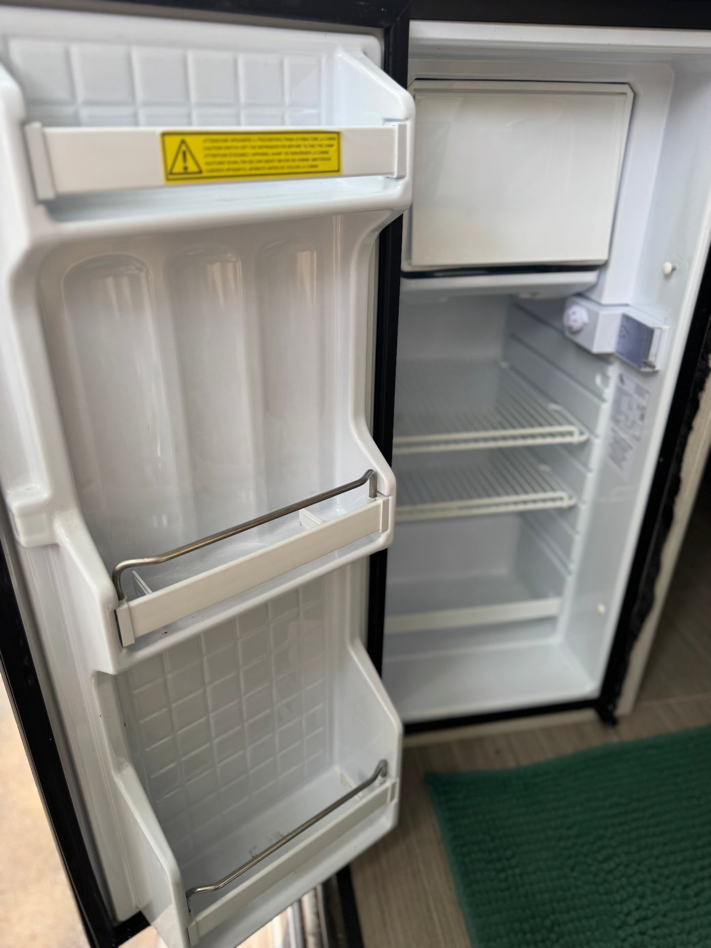 Empty, compact refrigerator inside an RV rental, showing internal shelves and door storage, ready for adventure supplies.