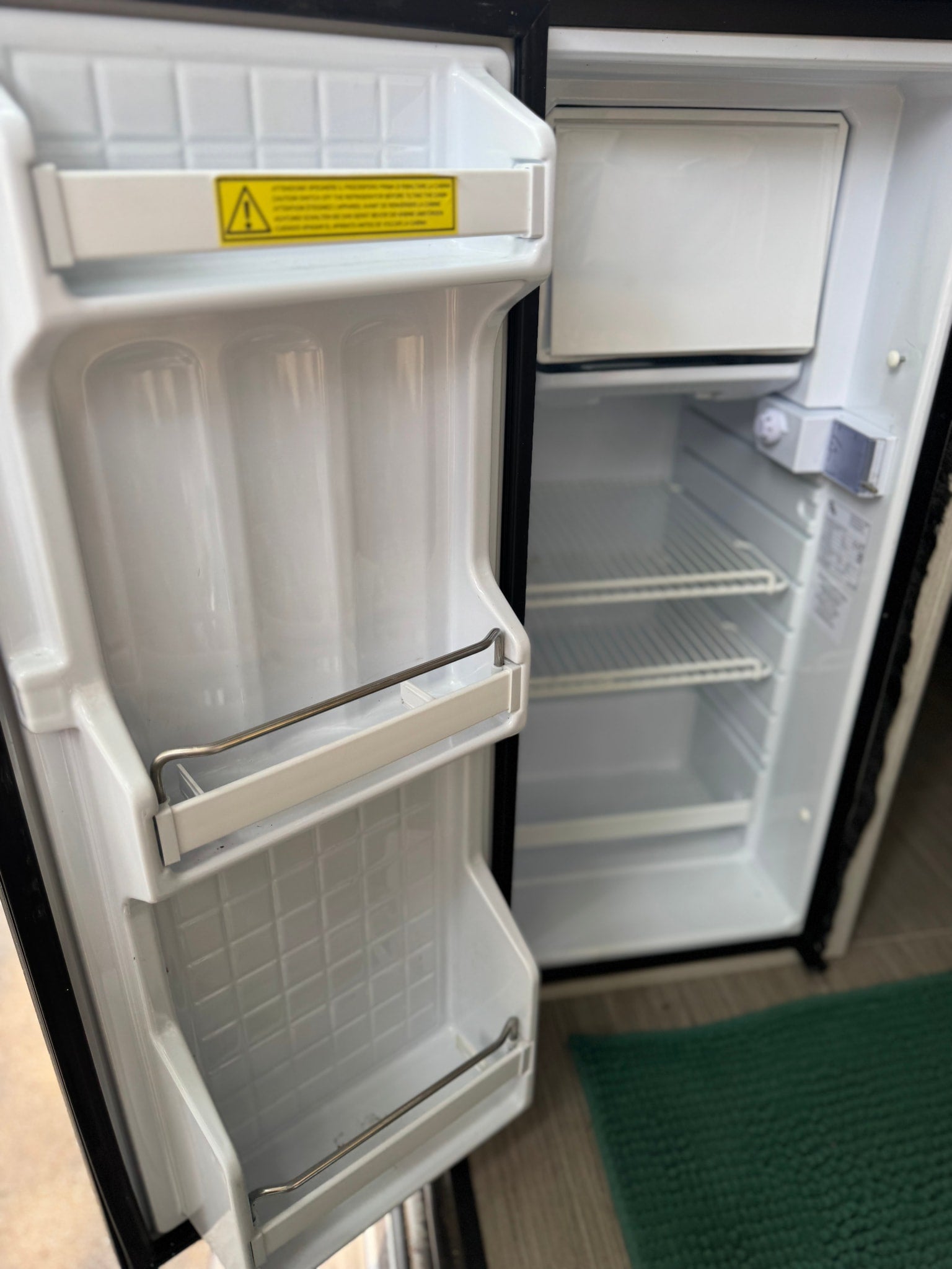 Empty, compact refrigerator inside an RV rental, showing internal shelves and door storage, ready for adventure supplies.