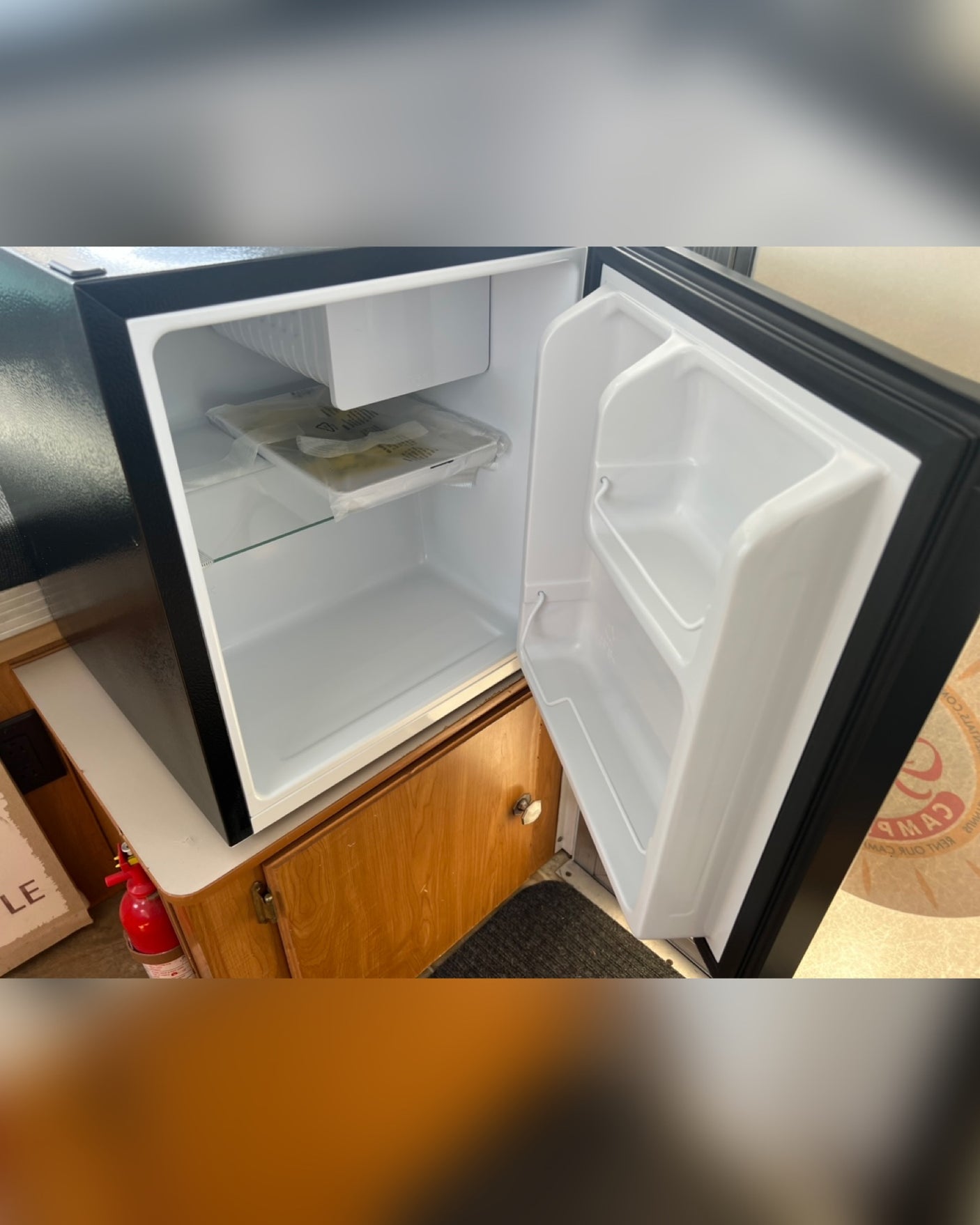 An open, compact black and white mini-fridge in an RV rental, showcasing its small freezer, shelf, and door storage.