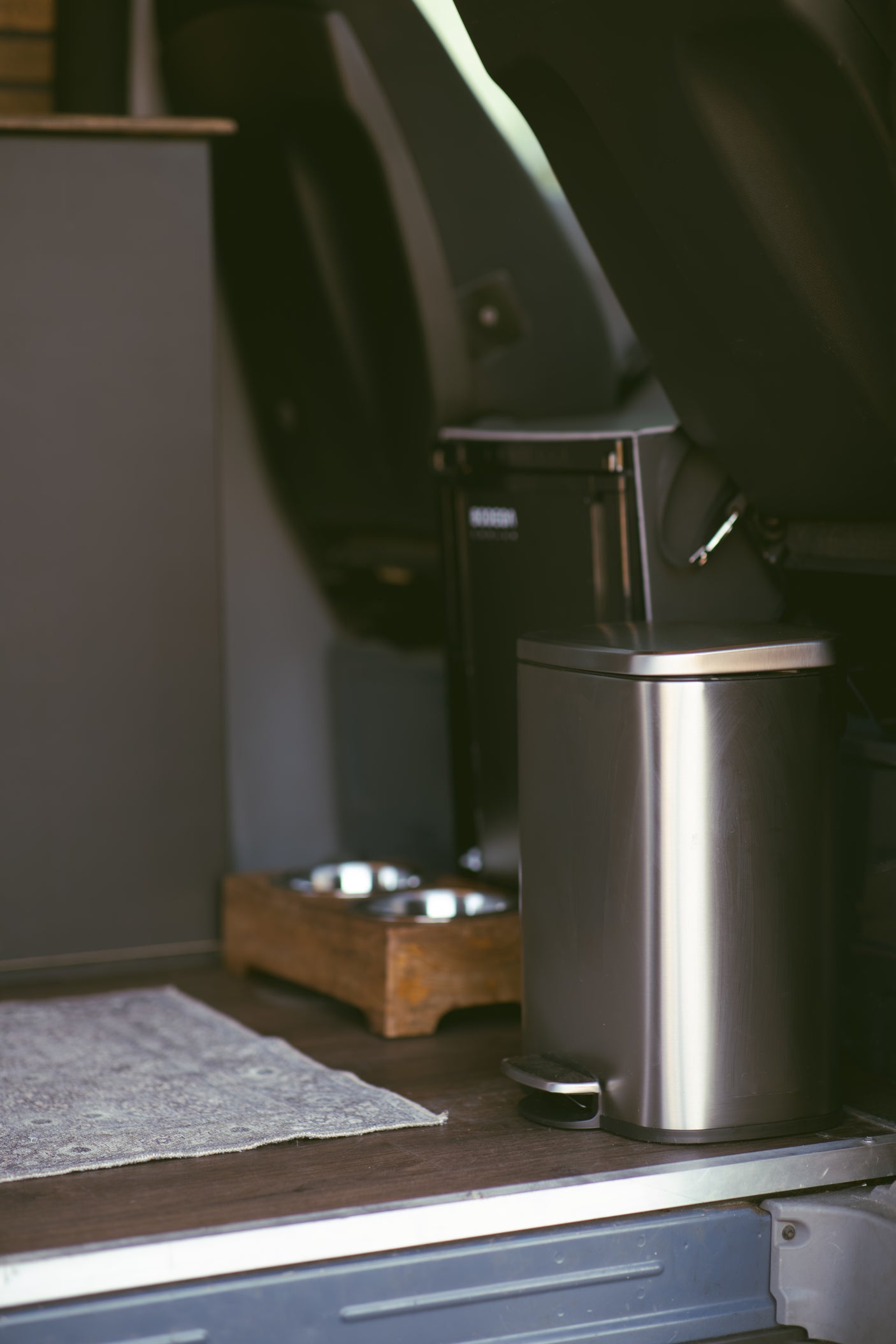 RV rental amenities: a stainless steel trash can, pet food/water bowls on a stand, and a floor mat. Functional interior.