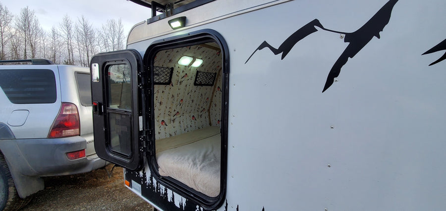 Cozy RV rental with open door revealing a bed, birch tree wallpaper, and lights inside. Ready for your next adventure.