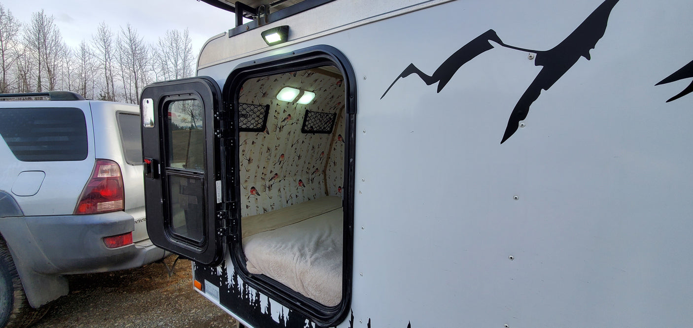 Cozy RV rental with open door revealing a bed, birch tree wallpaper, and lights inside. Ready for your next adventure.