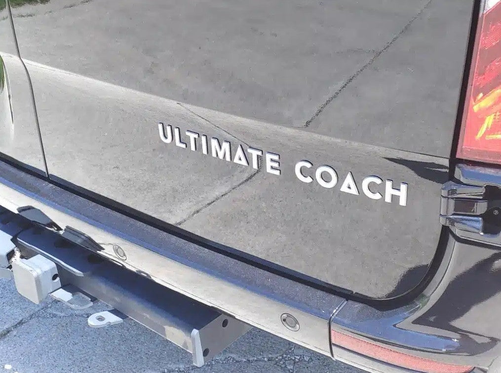 Rear of a dark Ultimate Coach RV, ideal for an RV rental. Features a tow hitch and bumper sensors.