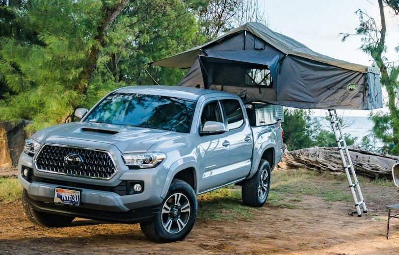 Grey Toyota Tacoma pickup with a rooftop tent set up for camping near the ocean. Perfect for your RV rental adventure.