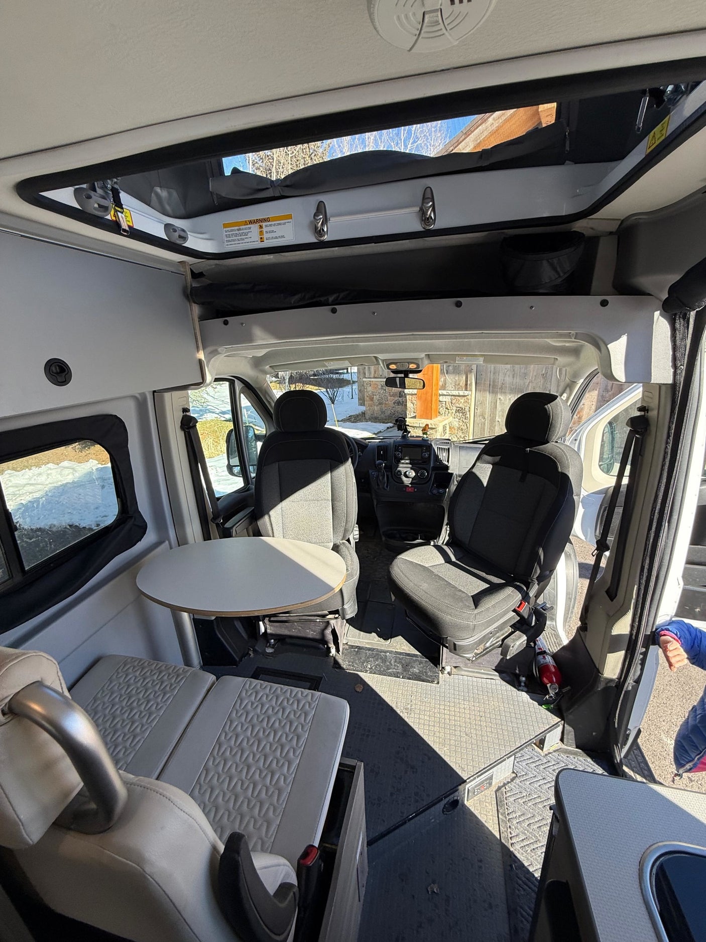 Inside this bright rv rental camper van, view of the cockpit, dining table, and living area. Features a pop-top roof.
