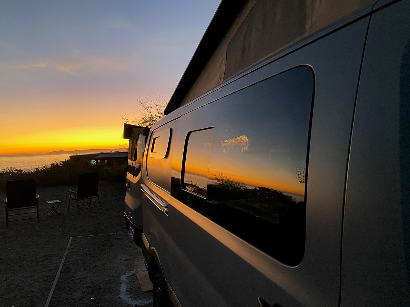 An rv rental camper van reflects a vibrant sunset over the ocean. Chairs await a peaceful evening view. — photo 3