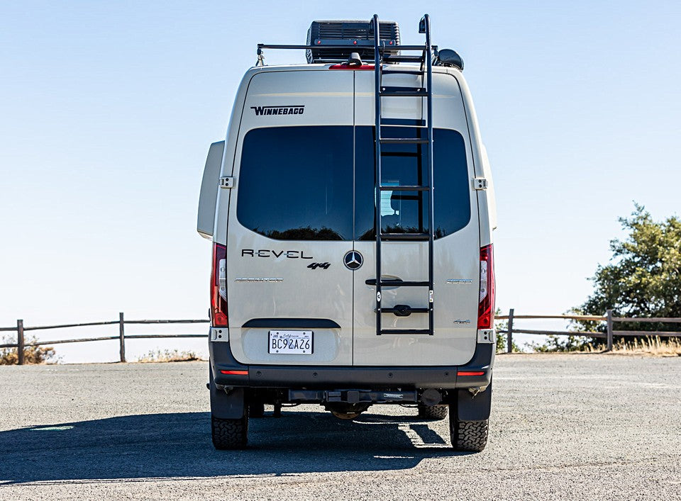 Rear of a beige Winnebago Revel 4x4 Sprinter camper van, an RV rental, with a rear ladder and roof rack.