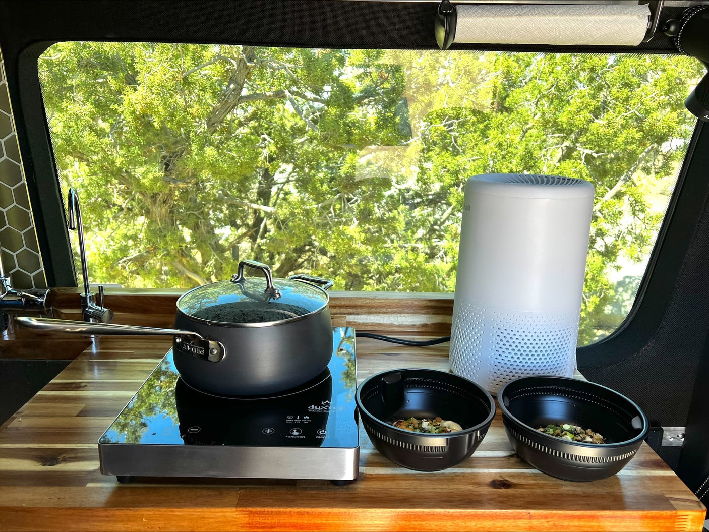 Inside an RV rental, a compact kitchen with an induction cooktop, pot, bowls of food, and an air purifier.