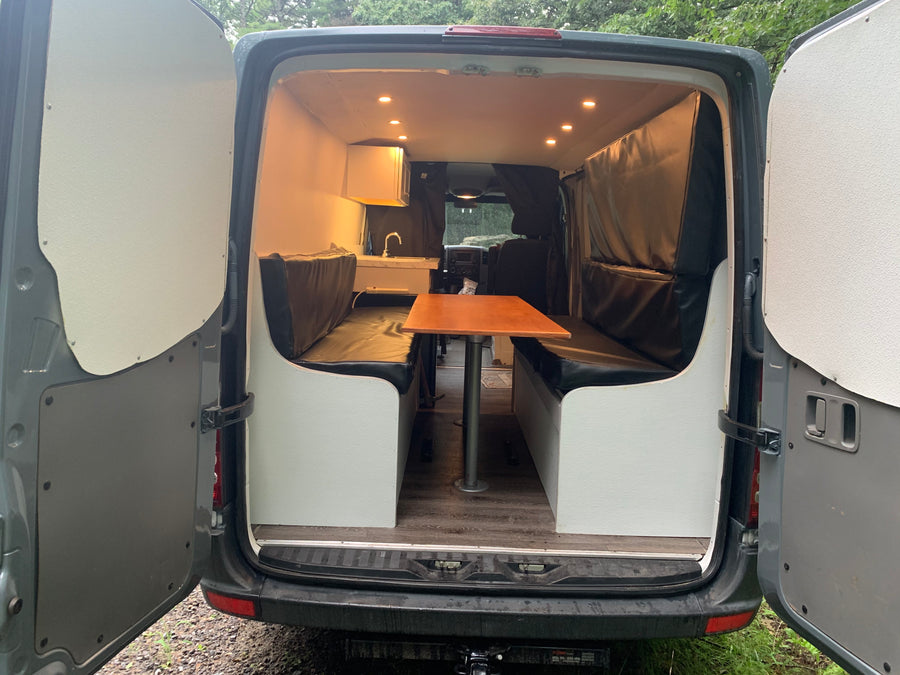 Explore this RV rental's cozy camper interior: dining area, sink, and warm lighting for your mobile adventures.