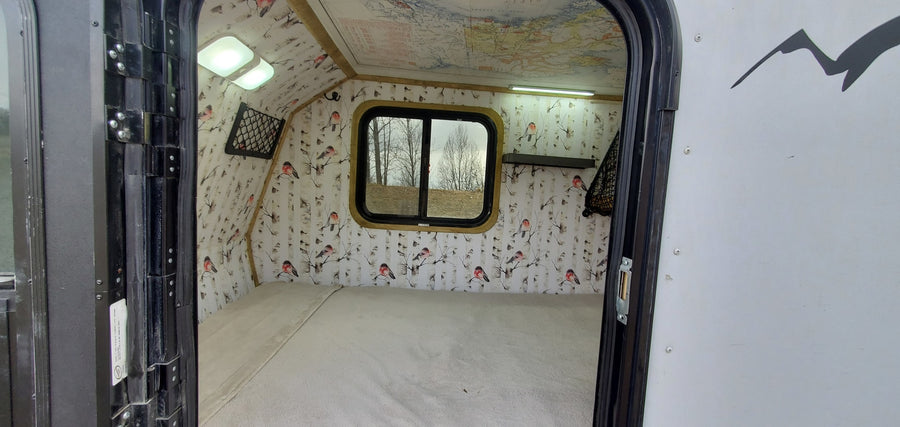 Explore this cozy RV rental interior: comfortable bed, unique bird & birch wall decor, map ceiling, and bright lighting.
