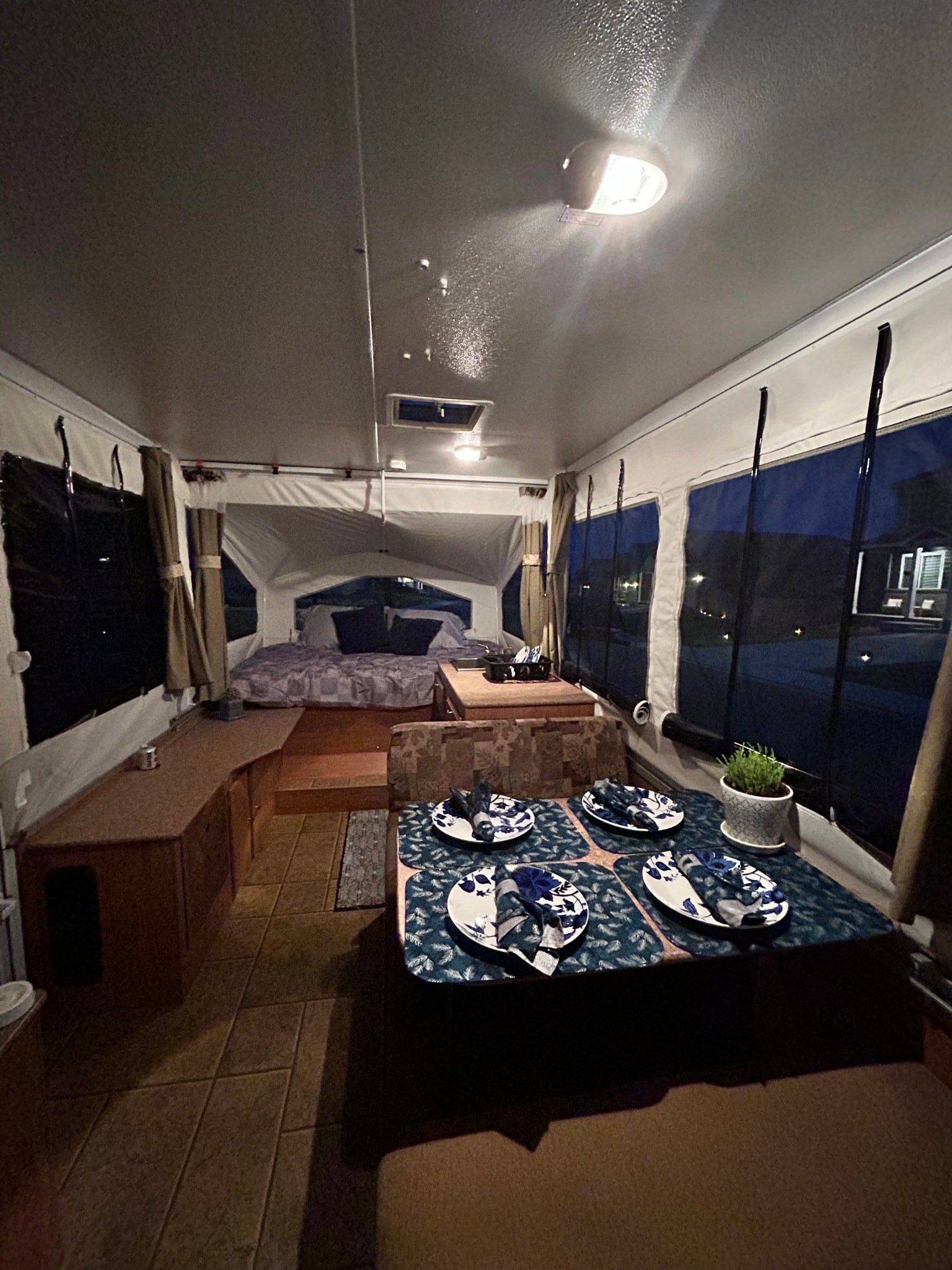 Step inside this cozy RV rental camper, featuring a neatly set dining area, comfortable bed, and warm lighting for a perfect getaway.
