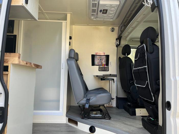 Spacious RV rental interior featuring a multi-functional living area with swiveling seats, fold-down table, and a compact shower stall.
