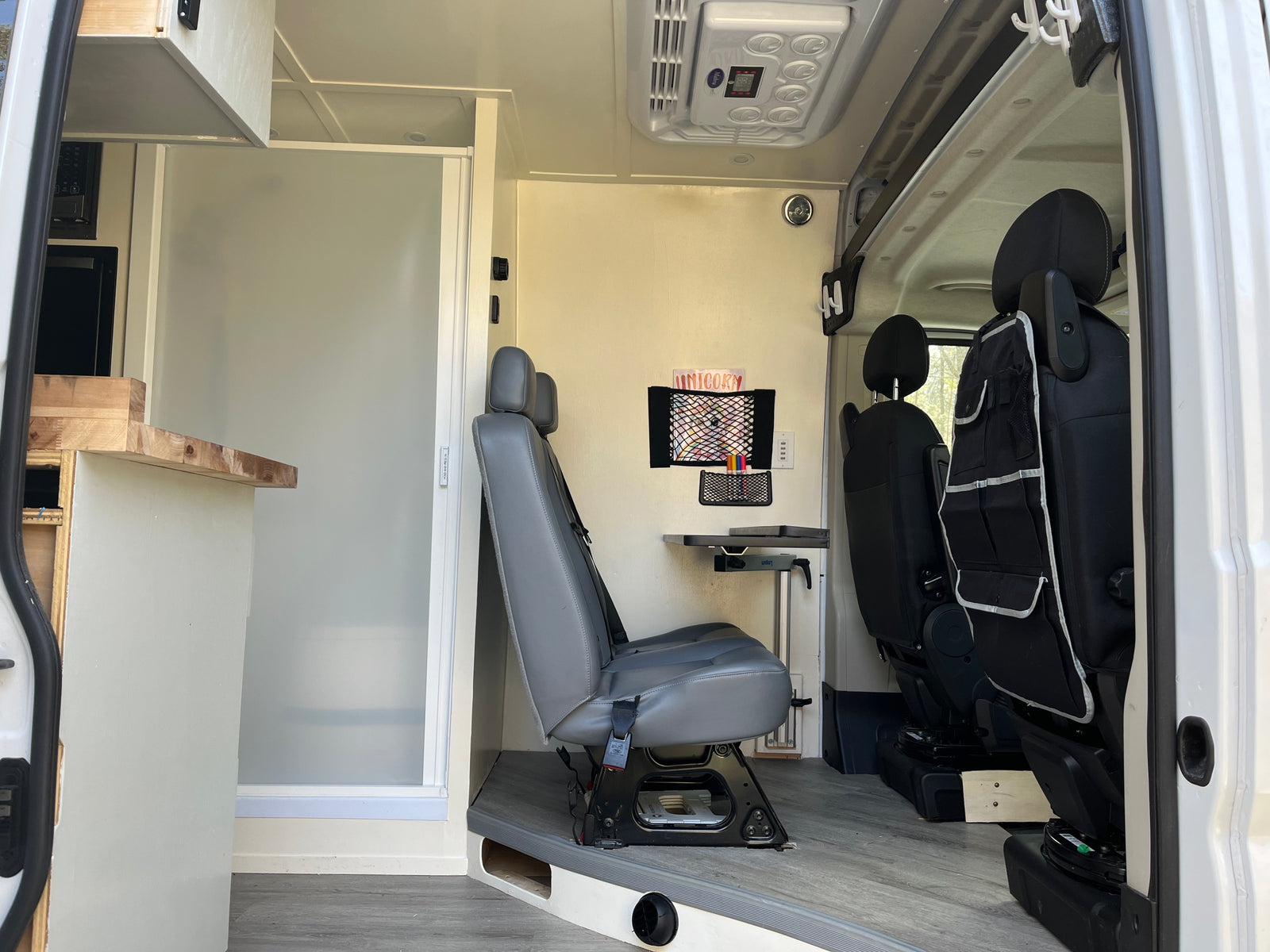 Spacious RV rental interior featuring a multi-functional living area with swiveling seats, fold-down table, and a compact shower stall.