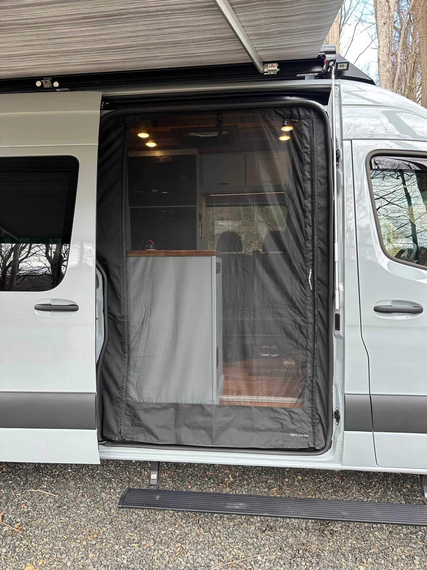 A light grey rv rental van, with its side door open, featuring a mesh screen and extended awning.
