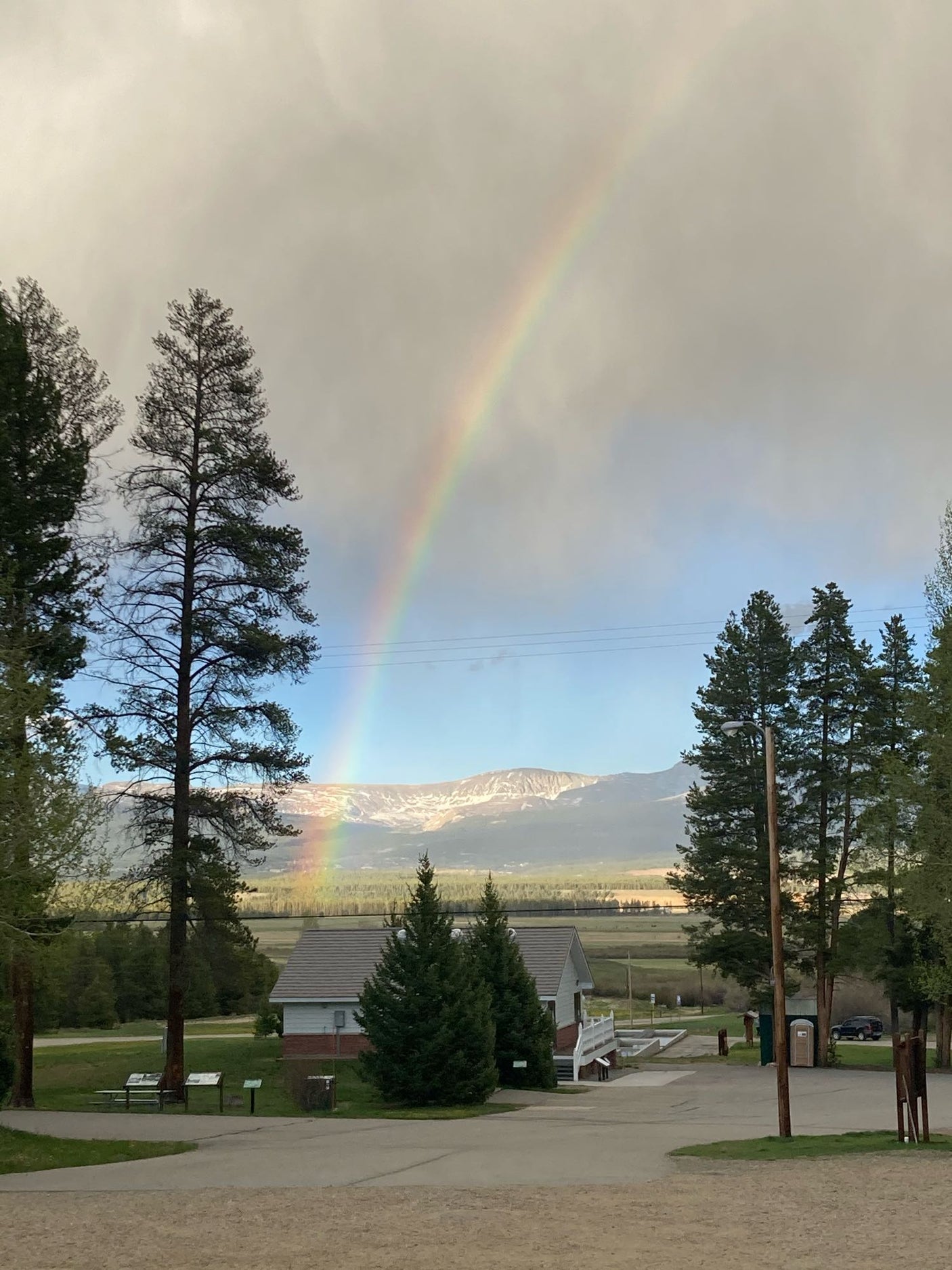 Stunning rainbow over snowy mountains and pine trees at a park, perfect for your RV rental adventure.
