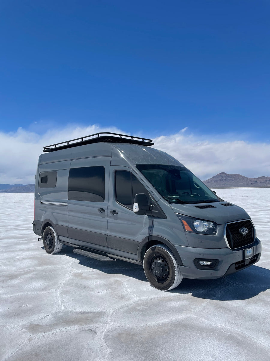 Gray Ford Transit camper van (RV rental) parked on the vast white salt flats under a clear blue sky.