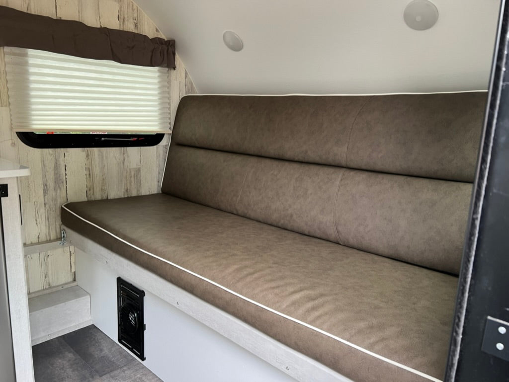Inside this cozy RV rental, find comfortable brown bench seating with a high back, pleated window shade, and light wood-look walls.