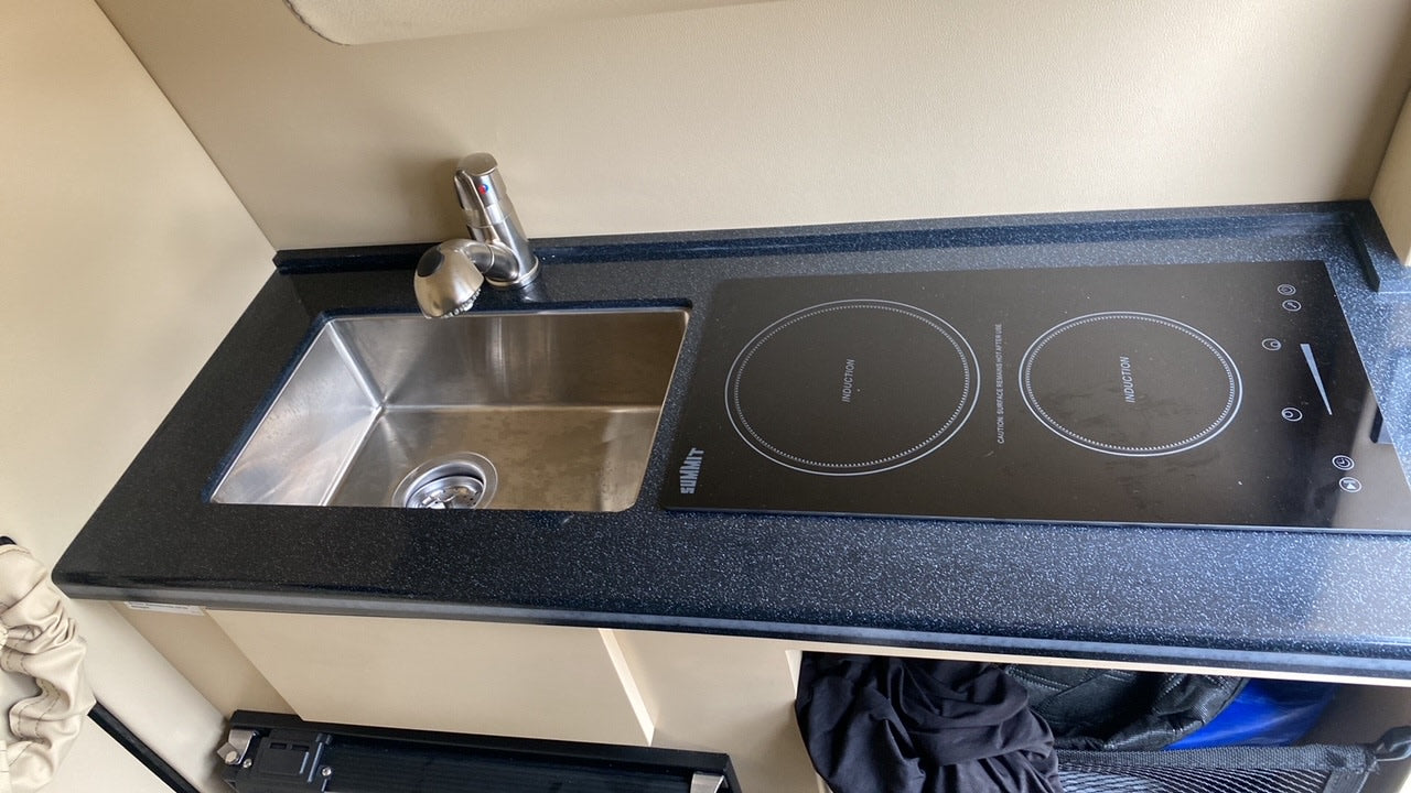 Compact kitchenette in an RV rental featuring a stainless steel sink, faucet, and two-burner induction cooktop on a dark counter.