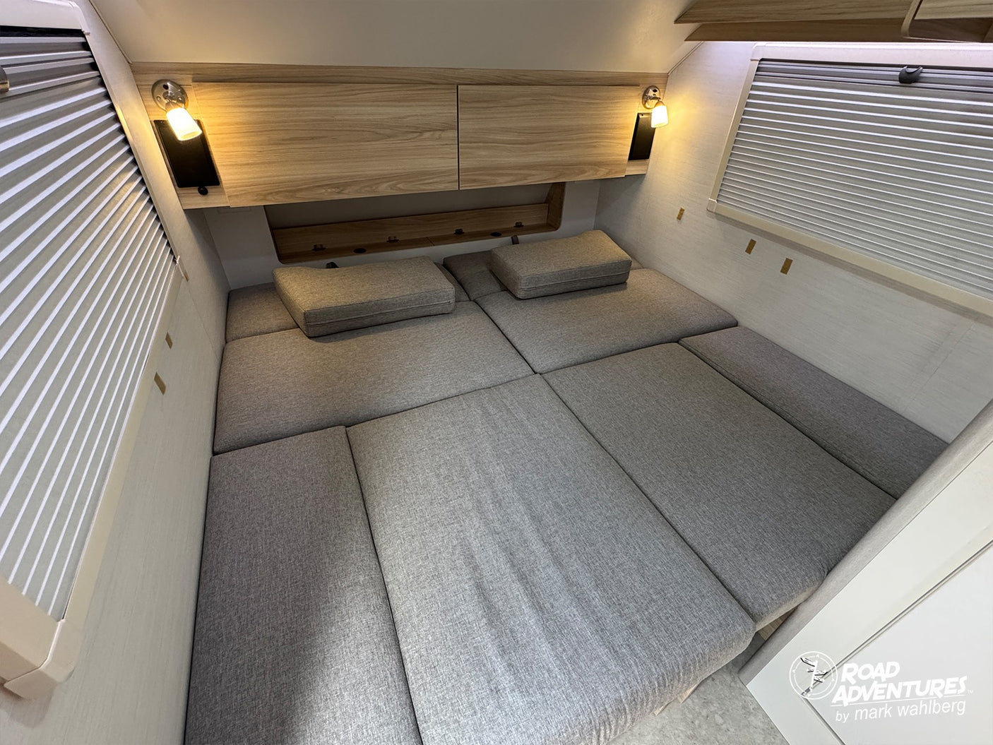 Comfortable rv rental sleeping area featuring gray cushioned bed, overhead wood storage, and bedside reading lamps.