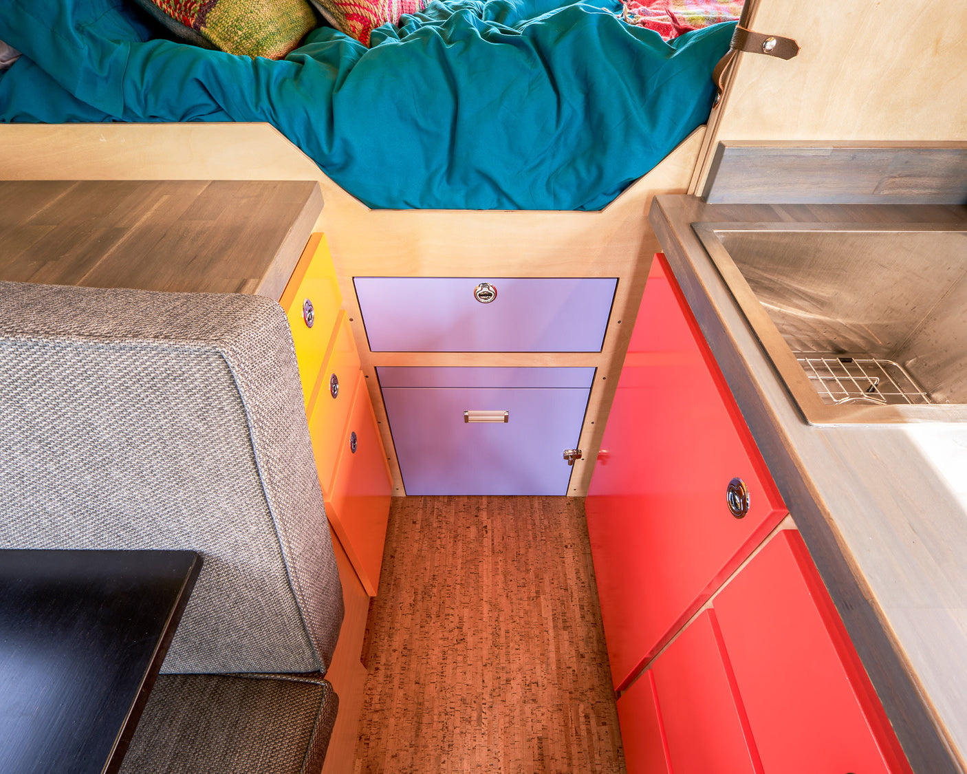 Colorful RV rental interior: cozy bed, compact kitchen with sink, bright storage cabinets, and comfortable seating.
