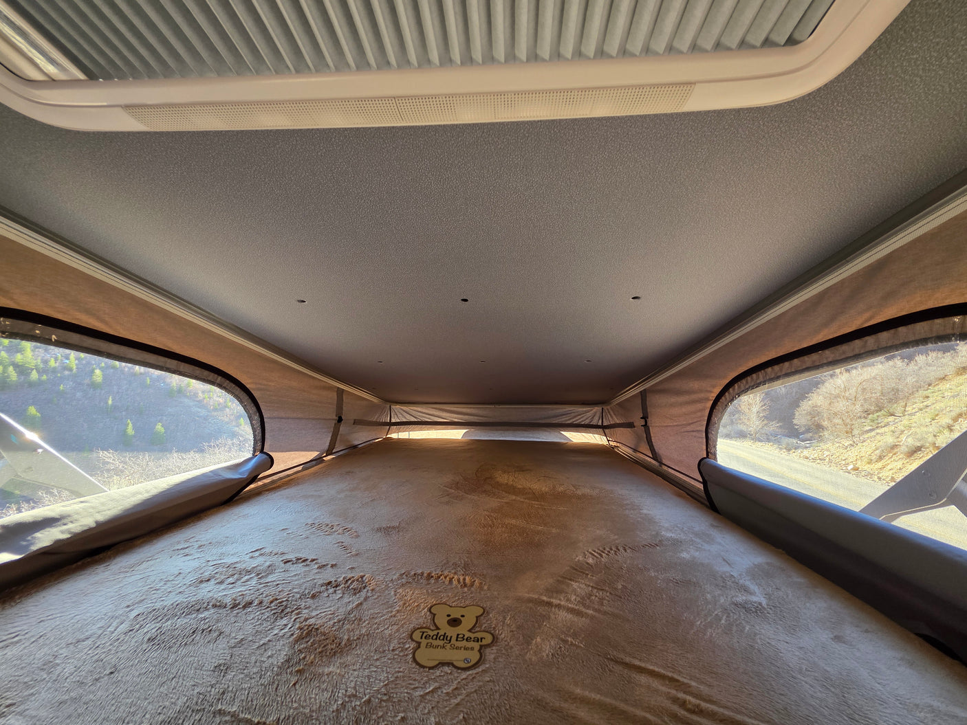 Inside a comfy RV rental pop-top bunk with a Teddy Bear mattress, offering scenic mountain views. Ideal for family travel.