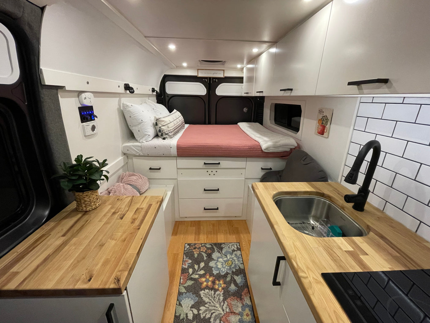 Cozy RV rental interior featuring a bed, butcher block countertops with sink/stovetop, and white storage cabinets.